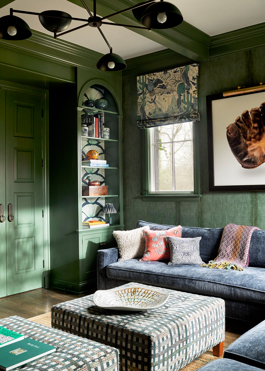 Green office with wallpapered shelving and seating with plaid striped ottomans. 