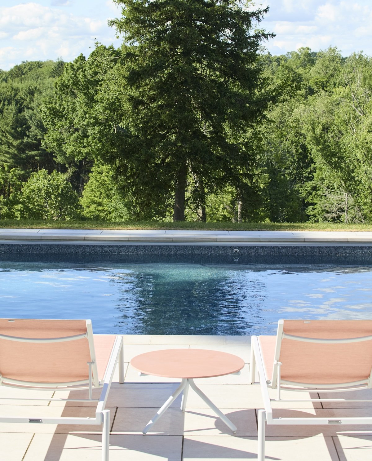 poolside view with blush lounge chairs tall trees lush hillside backdrop by betsy wentz design