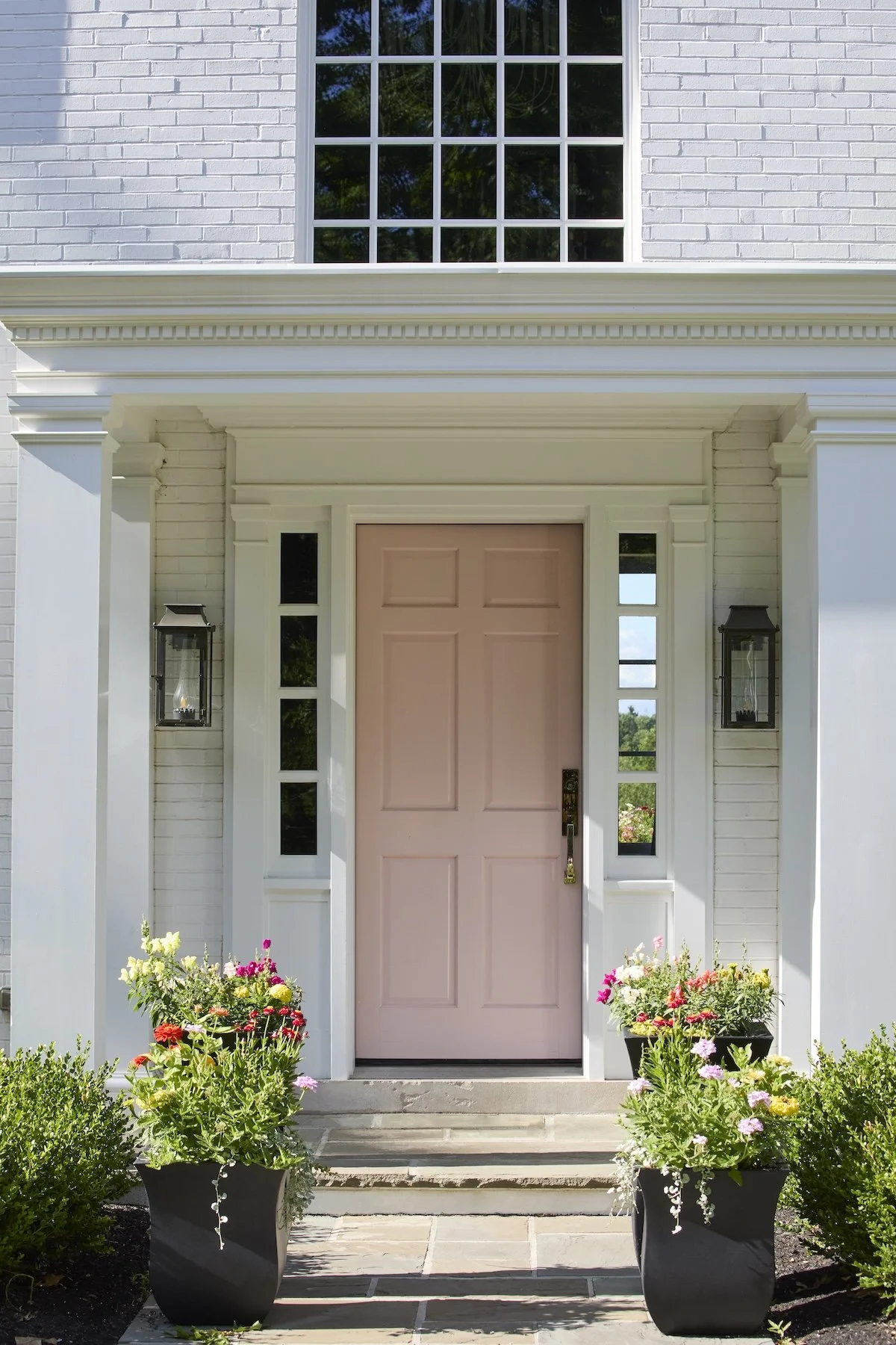 charming blush pink front door with white trim black lantern sconces black flower planters white brick colonial by betsy wentz design