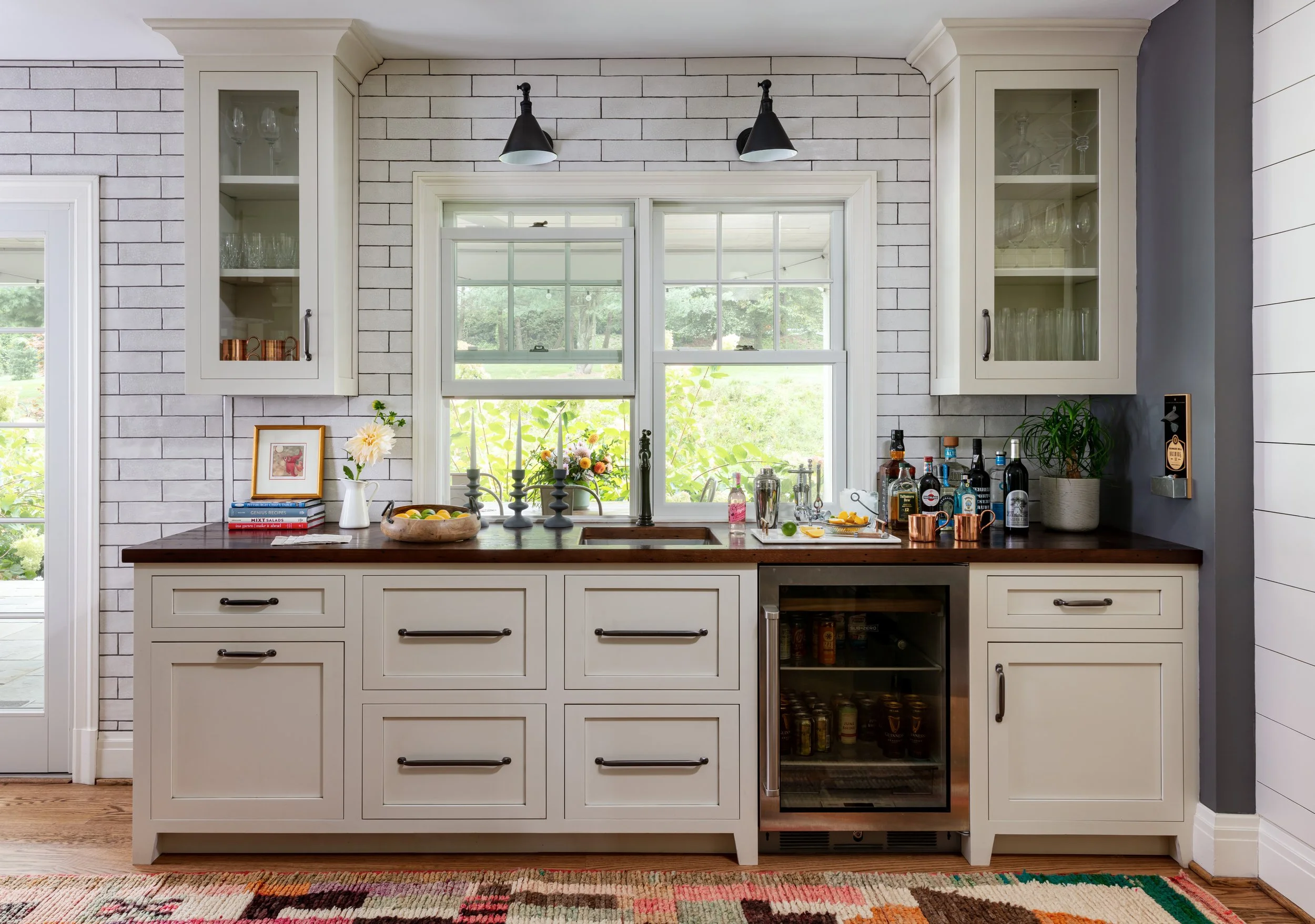 stylish modern kitchen wet bar with white cabinetry, dark wood countertop, glass doors, subway tile backsplash, and built-in wine fridge for chic home entertaining design inspiration.