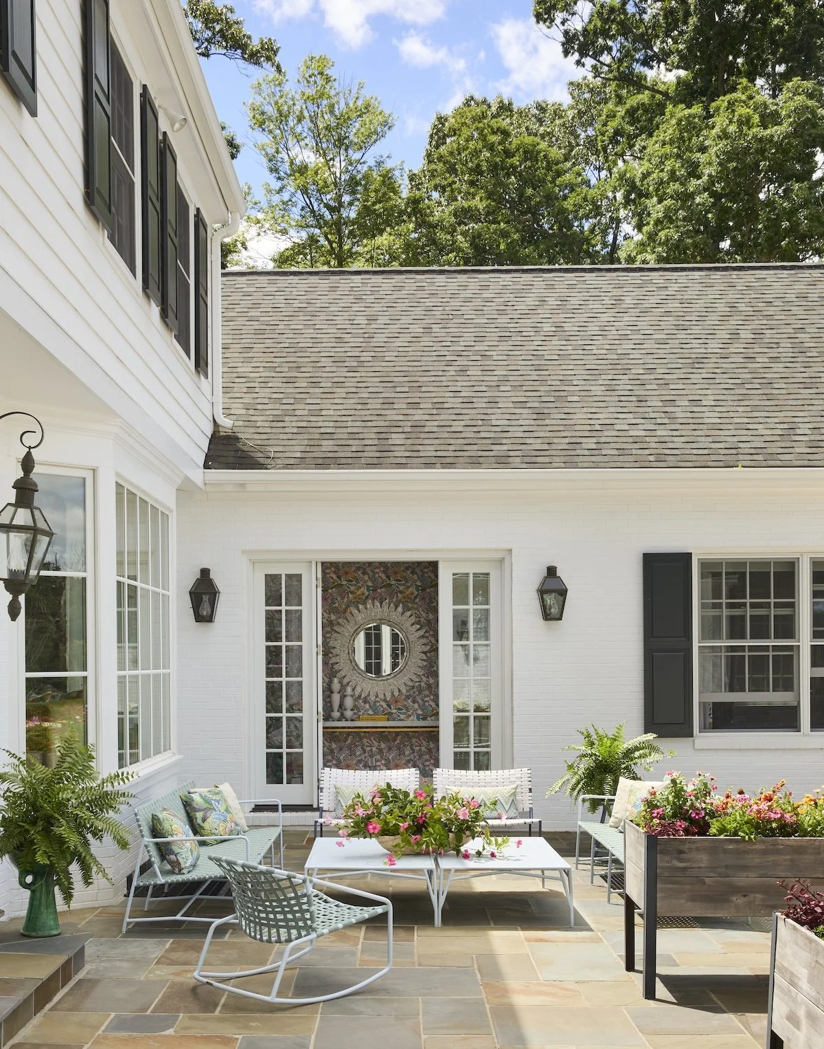 Charming back patio with light blue woven lounge chairs, stone pavers, pink floral centerpiece, sunburst mirror interior by Betsy Wentz