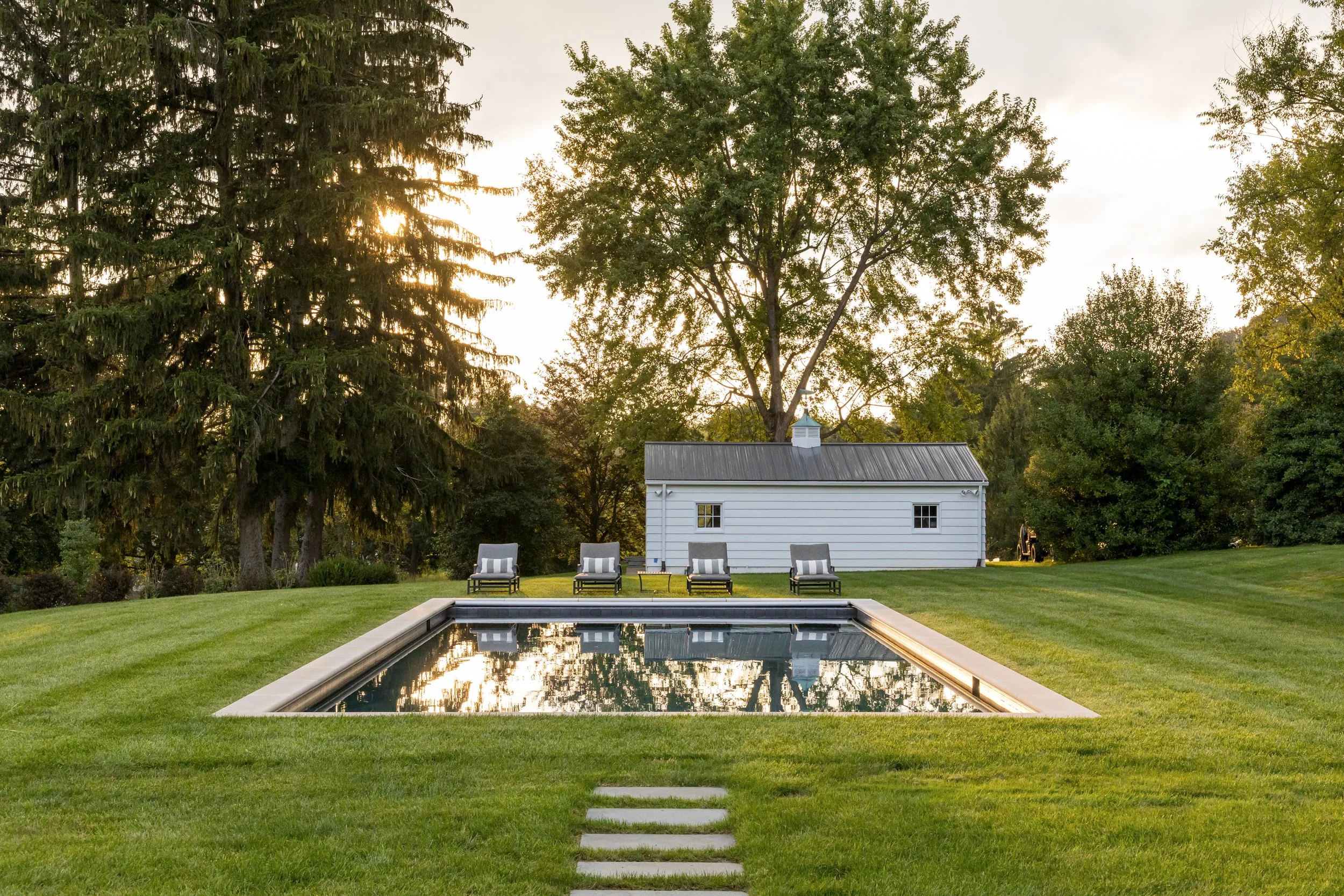Backyard infinity pool design with modern lounge chairs and rustic white shed for luxurious outdoor living and relaxation experiences