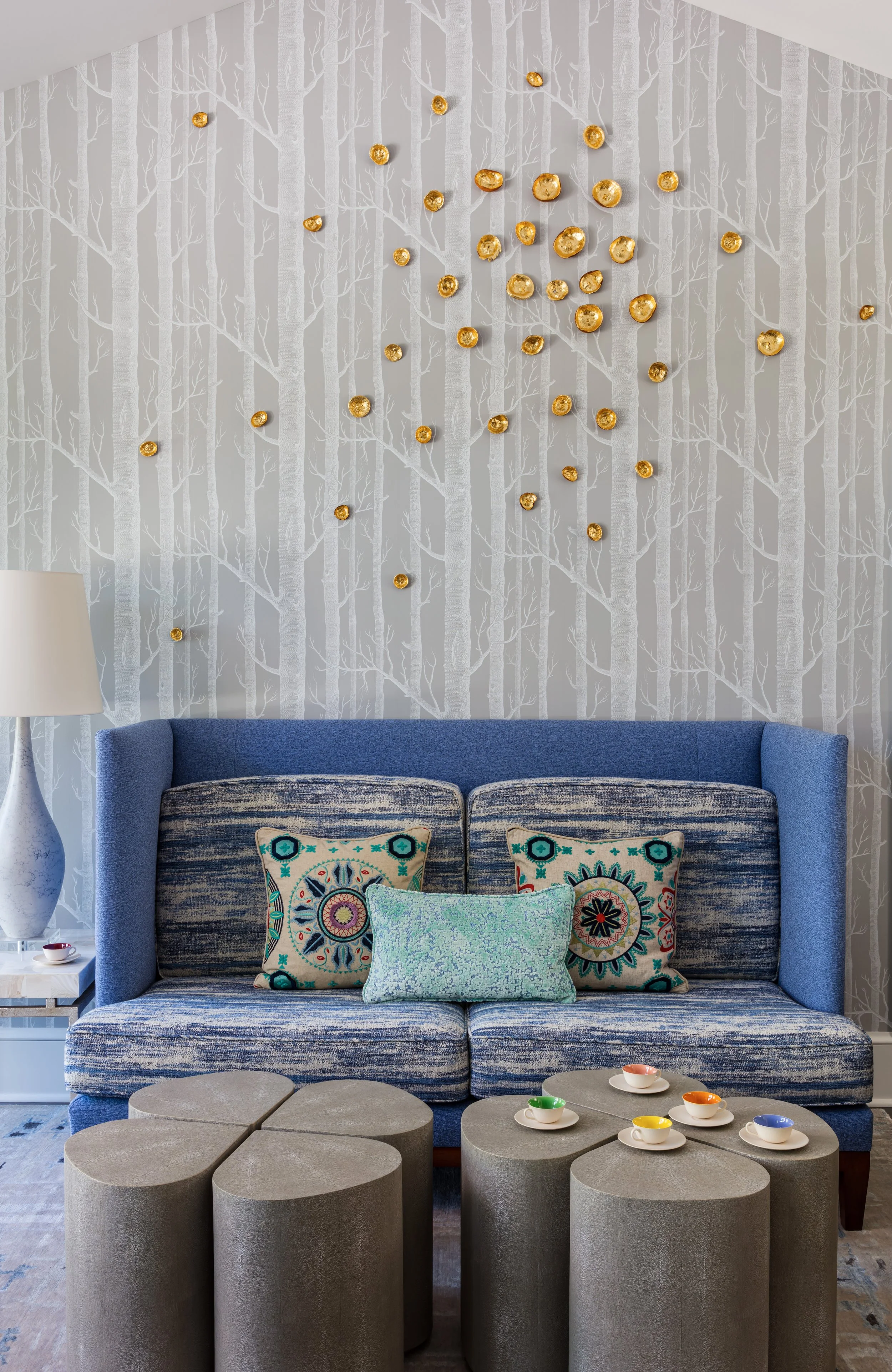 modern sitting area with blue sofa clover ottomans patterned wallpaper with gold art