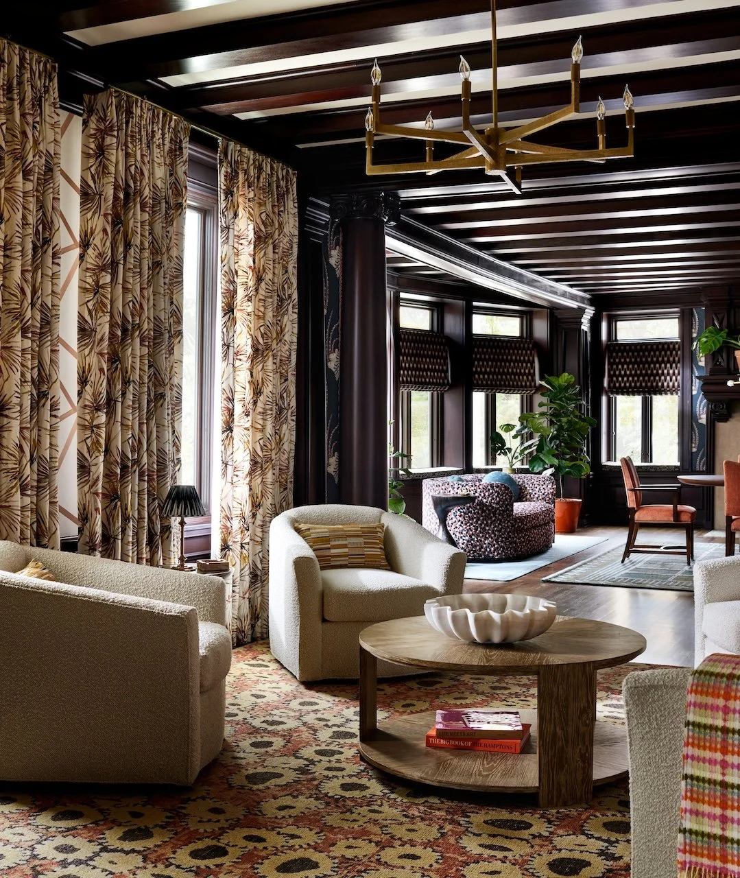 Conversation area beamed ceiling brass chandelier patterned drapes boucle chairs layered rugs flow