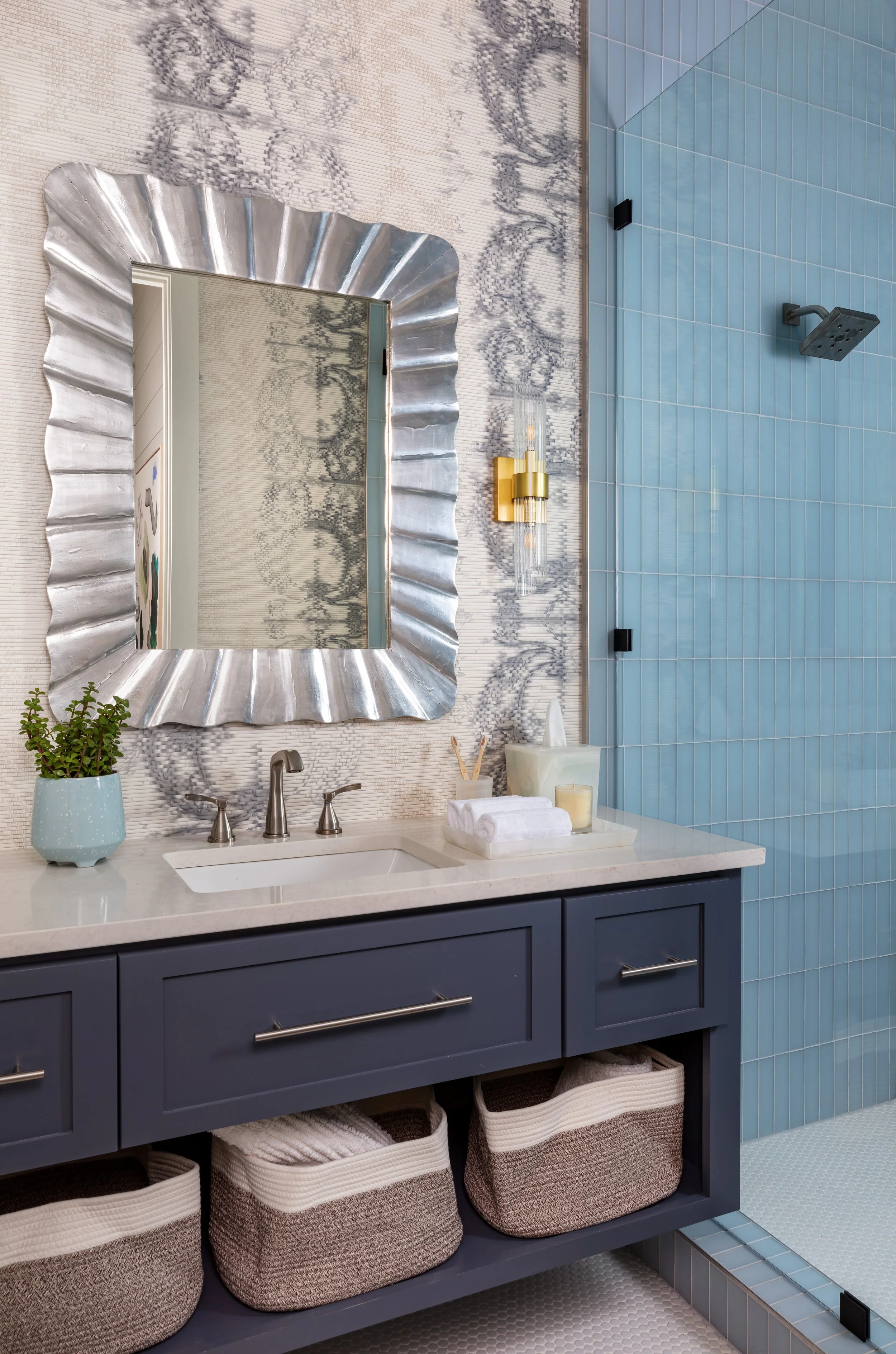modern bathroom with blue vanity, silver fluted mirror, marble wallpaper, blue tiled shower, and chic storage baskets for bathroom design inspiration