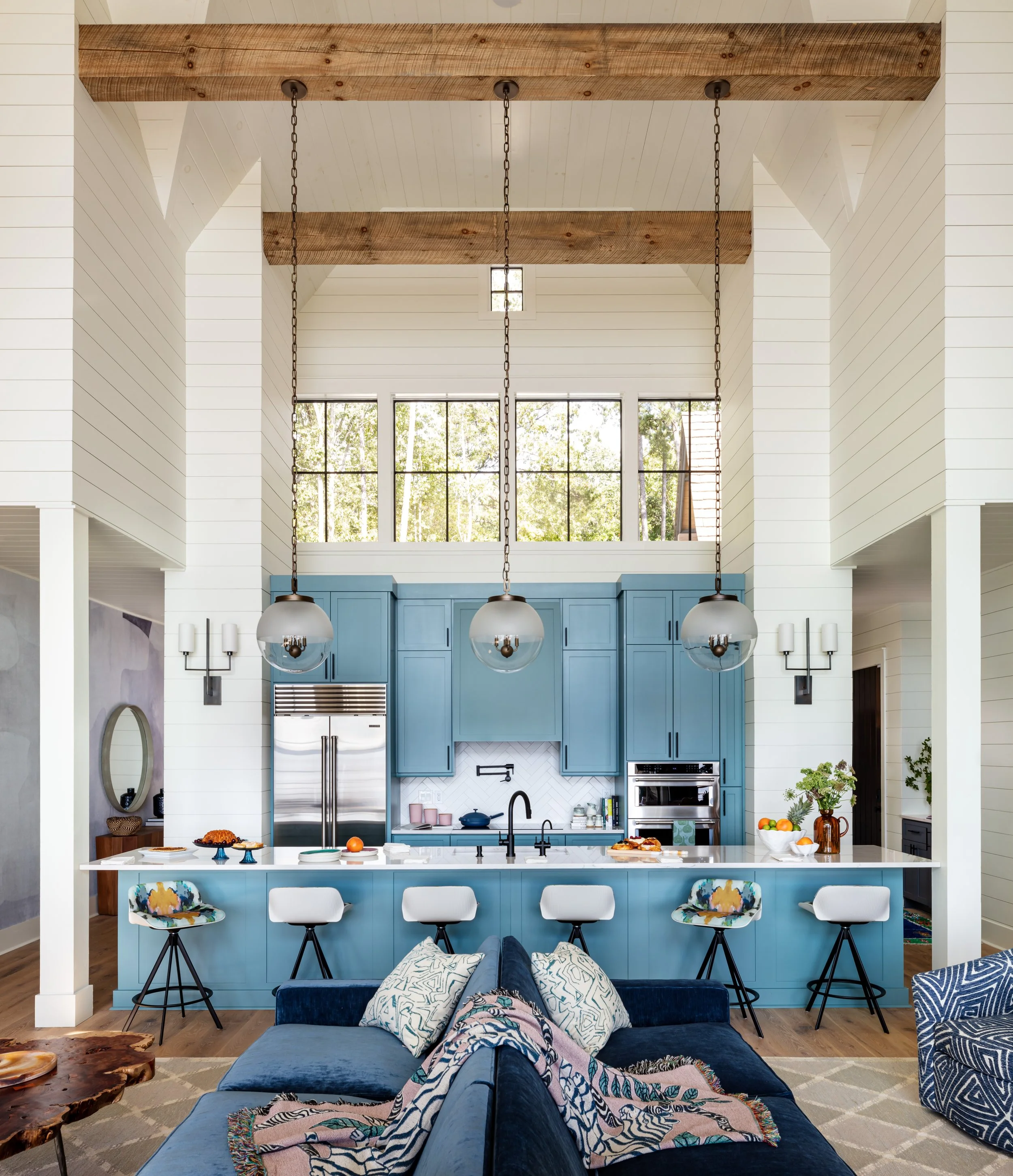 Modern open‑concept kitchen‑living space with blue island cabinets, white shiplap walls, exposed wood beams, pendant lights, and stylish seating for cozy, farmhouse-inspired interior design inspiration.