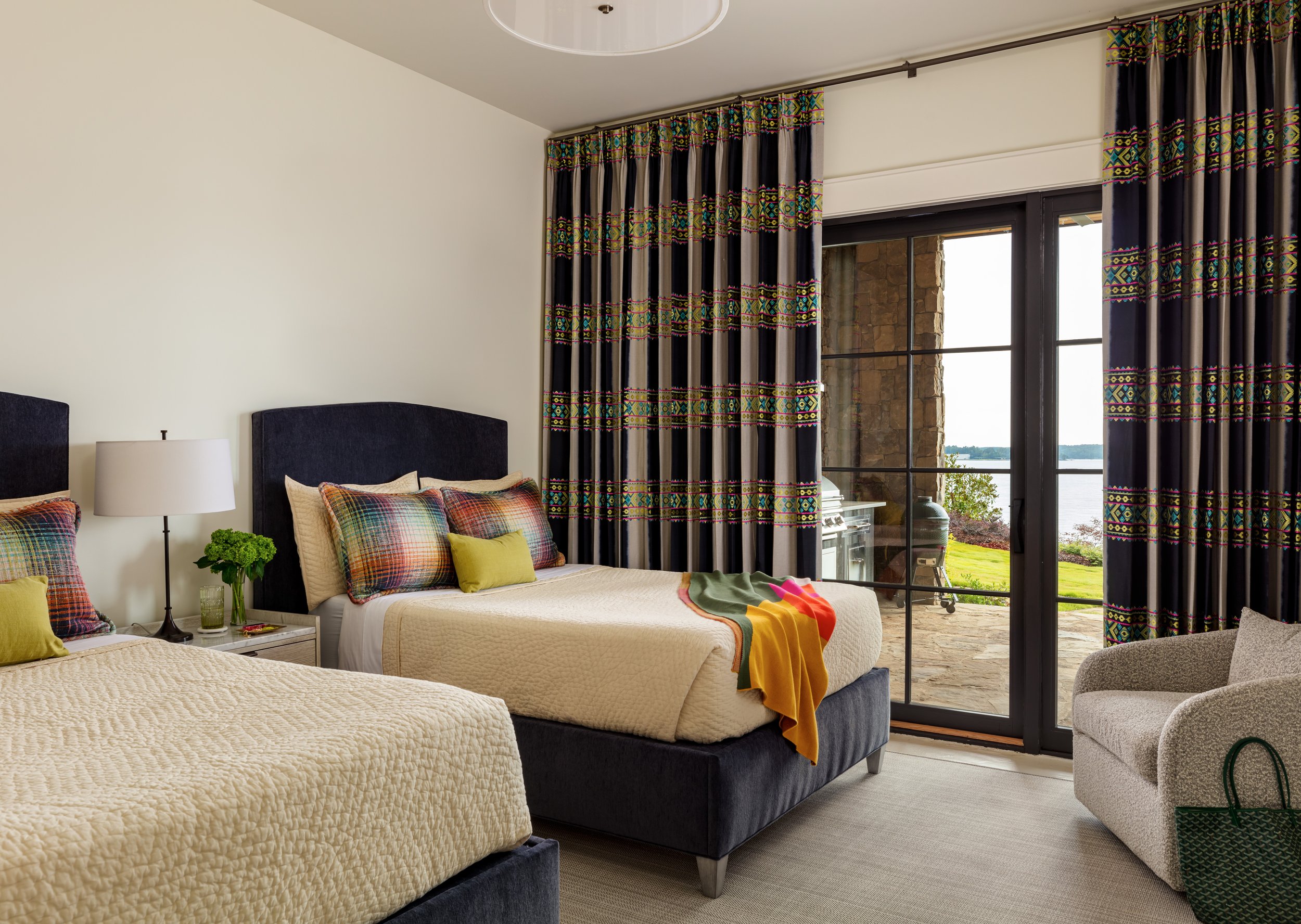 Stylish twin‑bed guest room with dark headboards, colorful plaid pillows, patterned curtains, and a patio view for cozy interior design inspiration