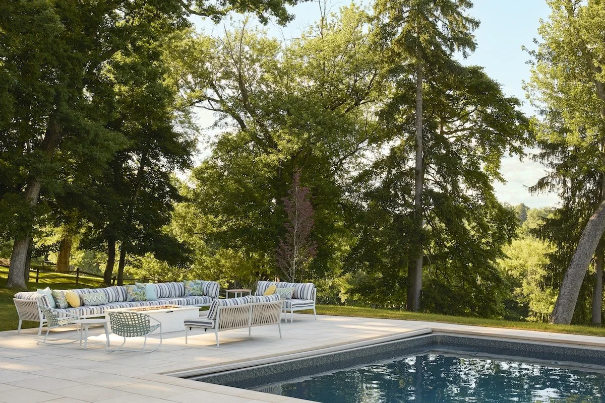 inviting poolside sectional with striped outdoor sofas woven chairs fire pit table tall trees sunny wooded view by betsy wentz design