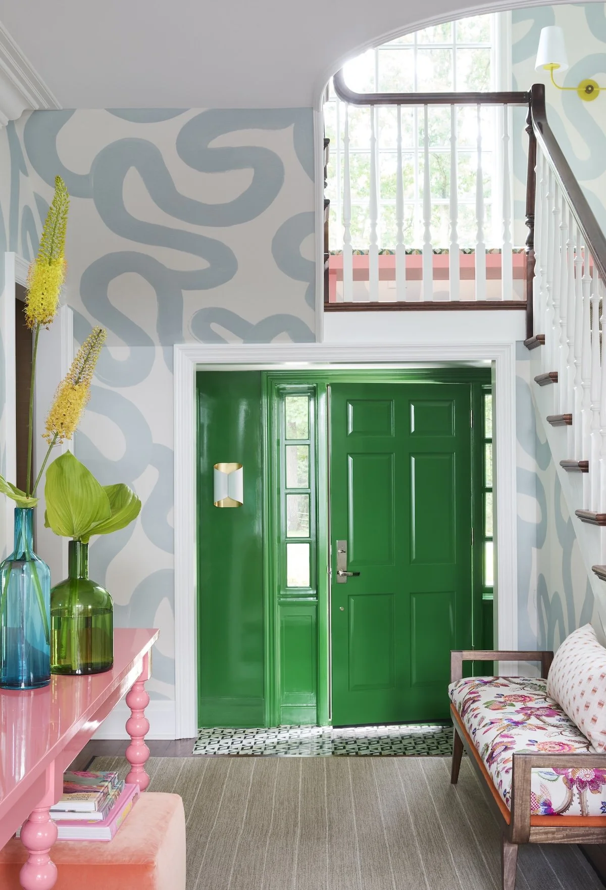 Vibrant entry foyer with emerald lacquered door, blue abstract wallpaper, pink console table, floral bench and patterned tile floor by Betsy Wentz