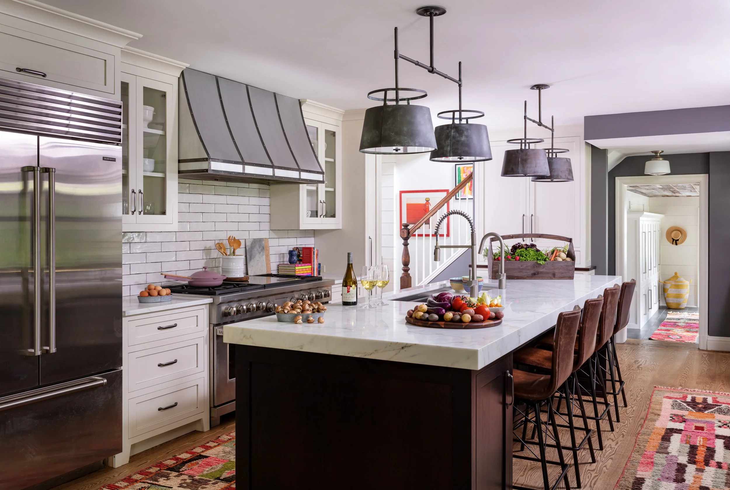 Modern kitchen design featuring white cabinets, stainless steel appliances, island with white countertop, pendant lights, and colorful patterned rug for stylish home interiors