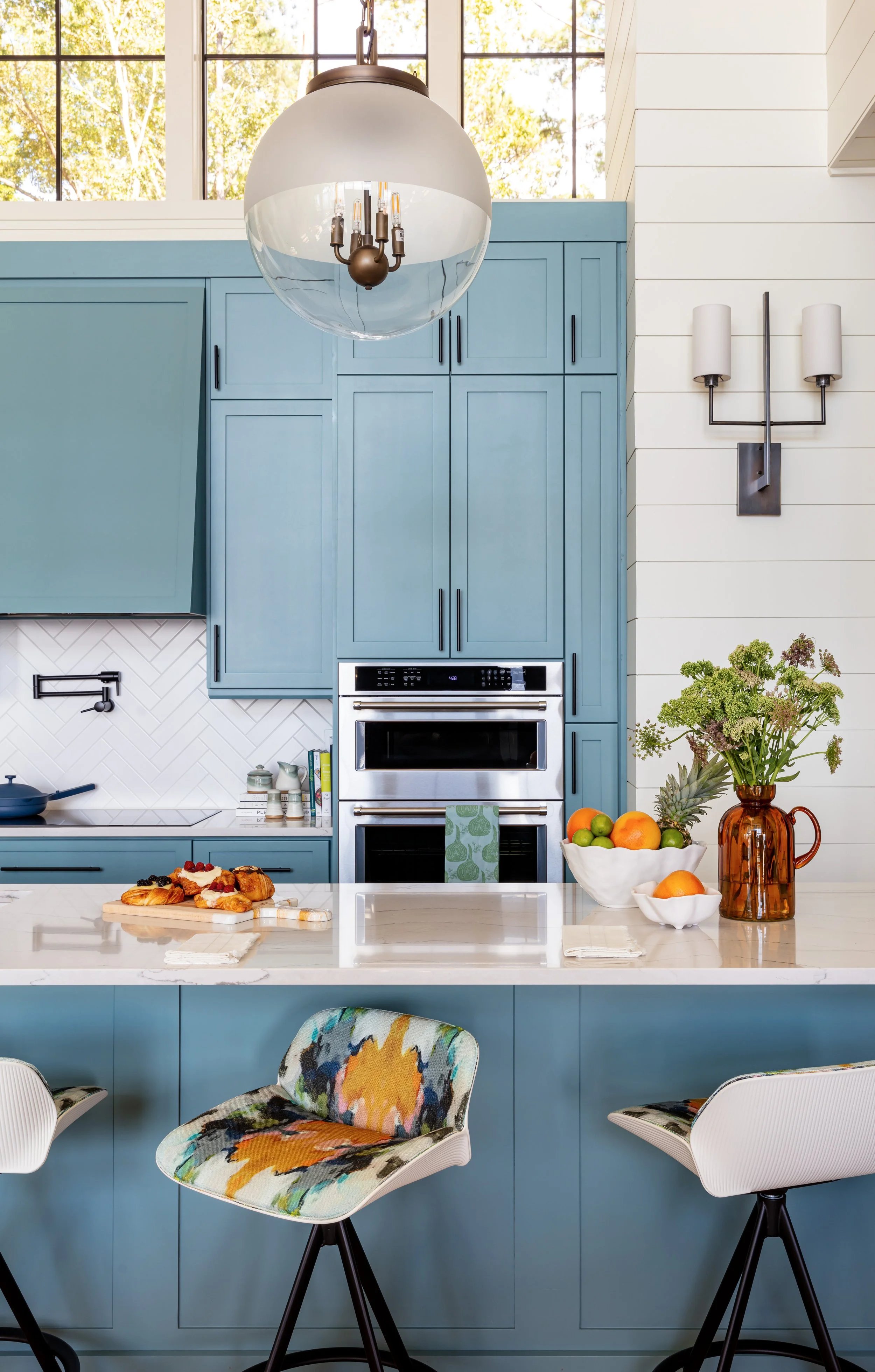 Modern open‑concept kitchen with blue island cabinets, white shiplap walls, globe pendant lights over island with counter stools, farmhouse-inspired interior design inspiration