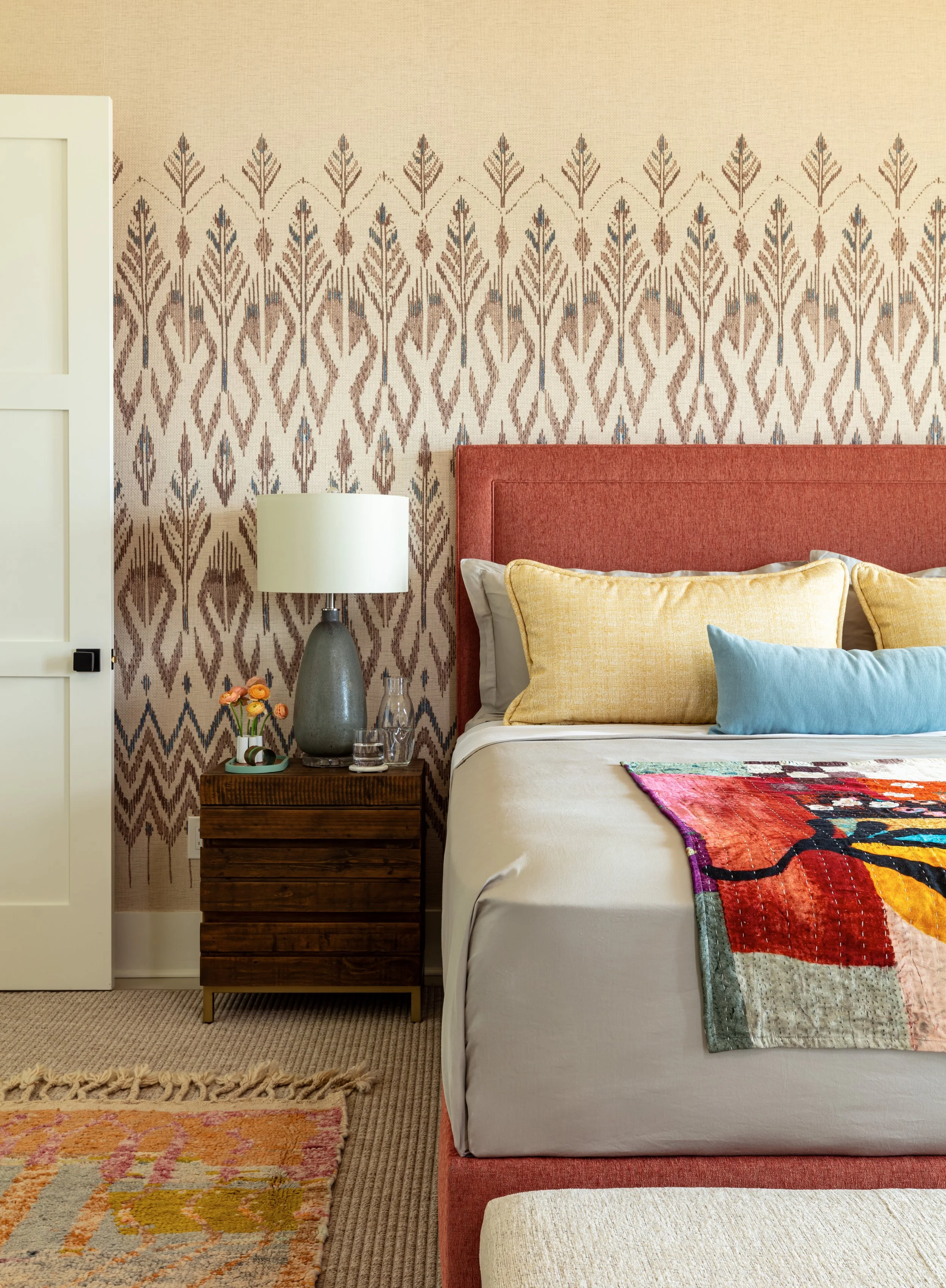 bedroom with upholstered bed, patterned wallpaper, colorful throw, modern lamps, and nighstand
