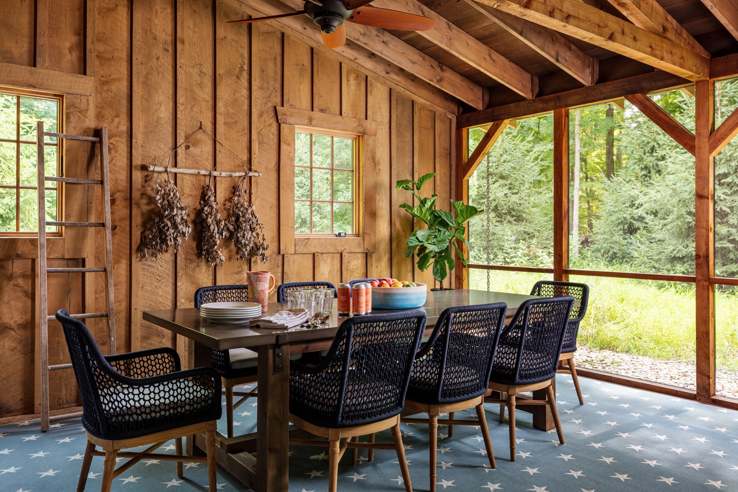 rustic-wooden-screened-porch-dining-area-with-ceiling-fan-and-natural-light-showcasing-modern-black-wicker-chairs-around-a-brown-table-decorated-with-fruit-bowl-and-plants-for-cozy-outdoor-entertaining-and-interior-design-inspiration.jpg