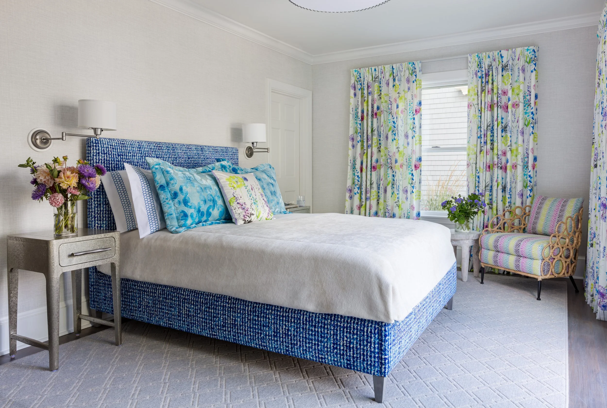 vibrant blue upholstered bed with white linens, colorful patterned curtains and accent chair create a stylish bedroom design 