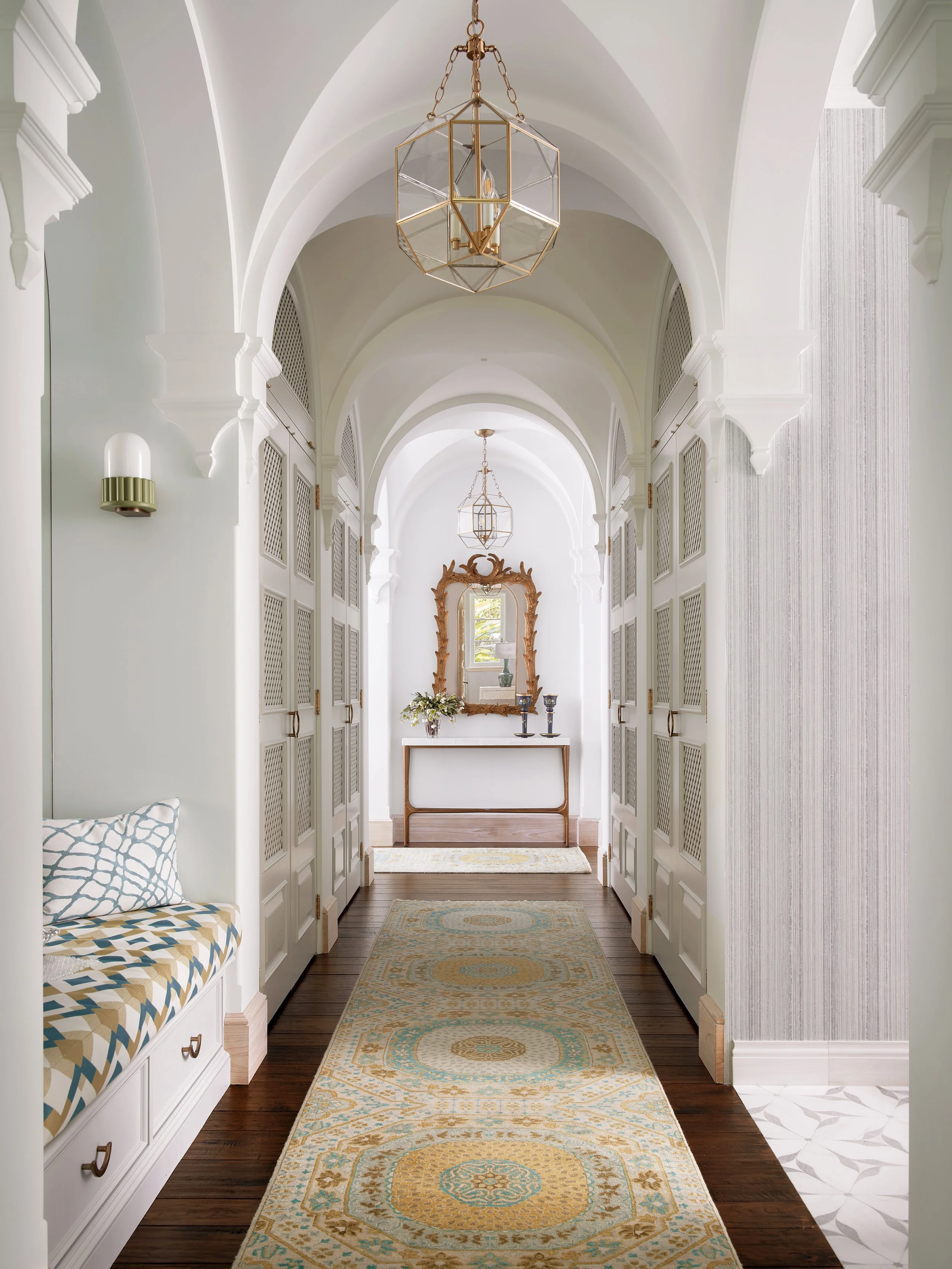 archway hallway with patterned rug white louvered doors brass chandelier wooden floor mirror console