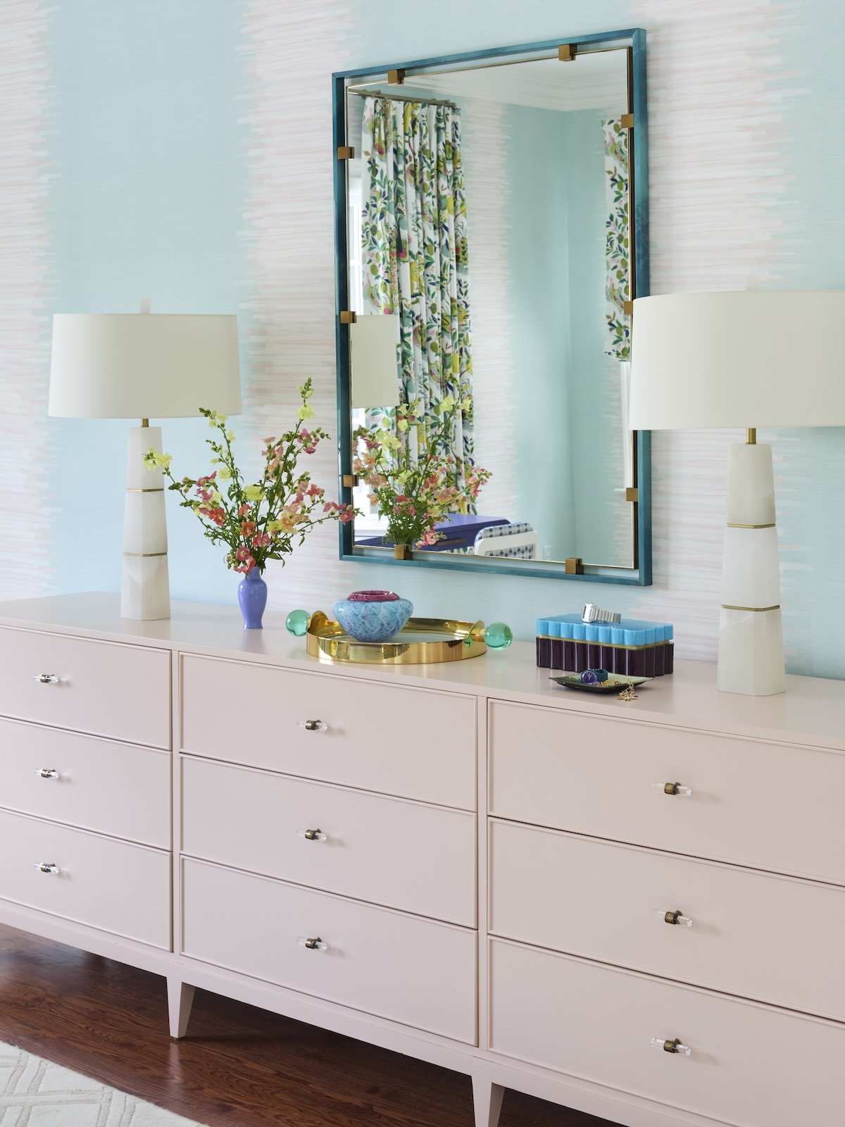 colorful primary bedroom dresser vignette with blush pink dresser aqua ikat wallpaper teal mirror alabaster table lamps