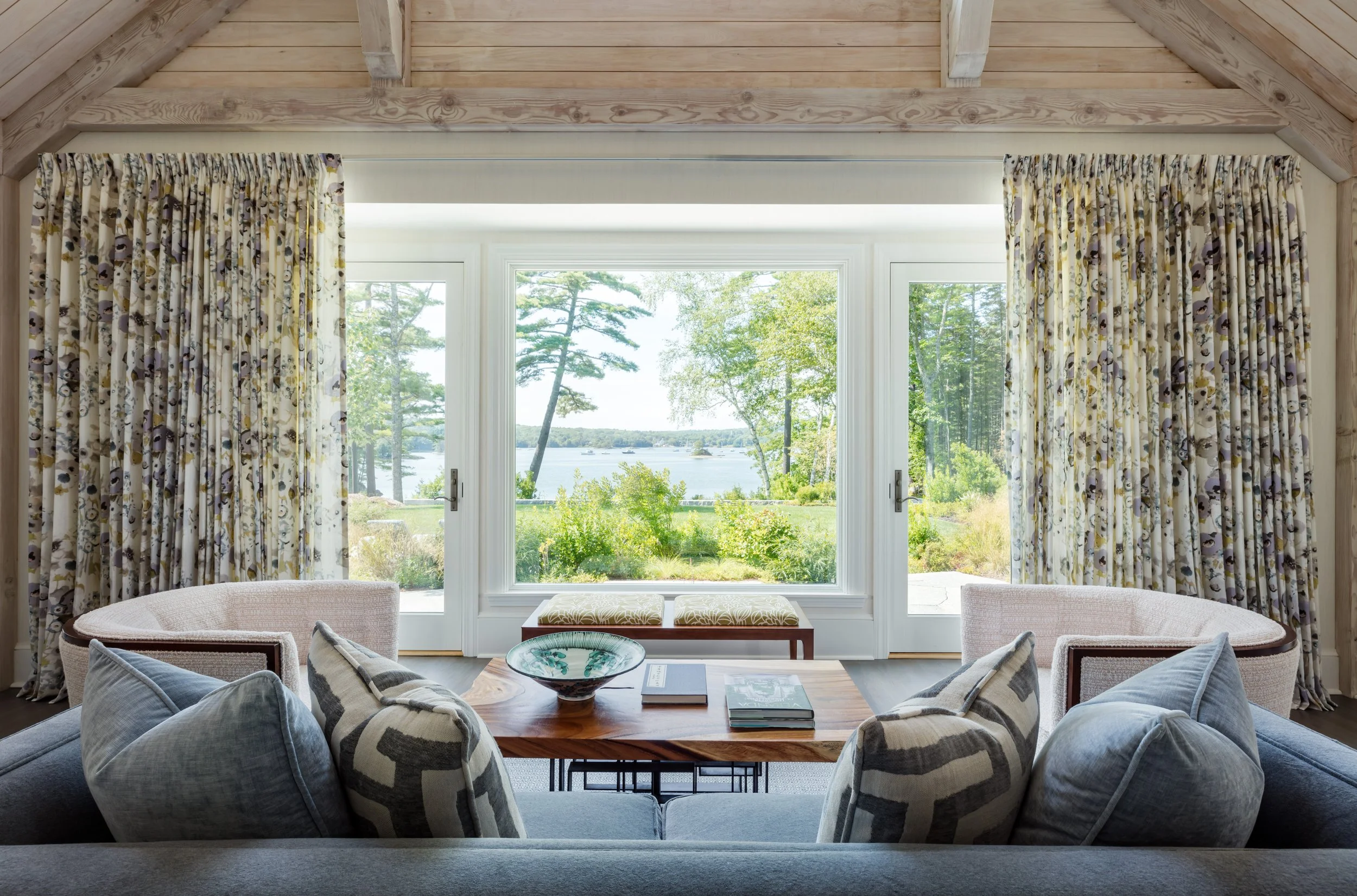 elegant waterside living room with vaulted wood ceiling, floral drapery for large window, gray sofa stylish furnishings for cozy retreat
