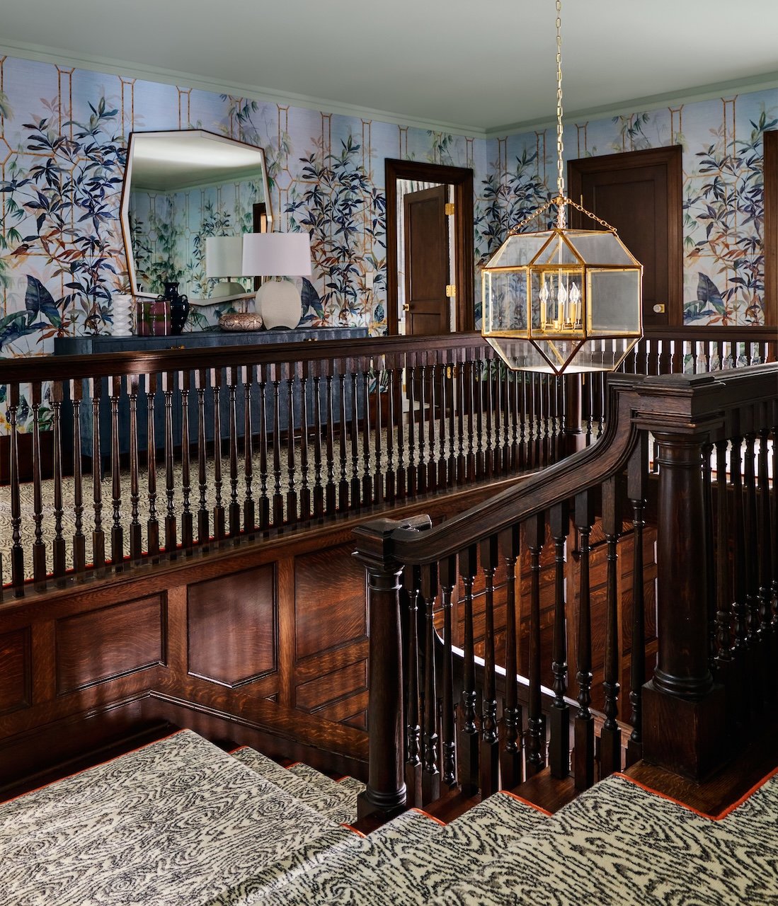 Traditional stair landing with chinoiserie wallpaper dark wood railing brass lantern patterned runner and blue console