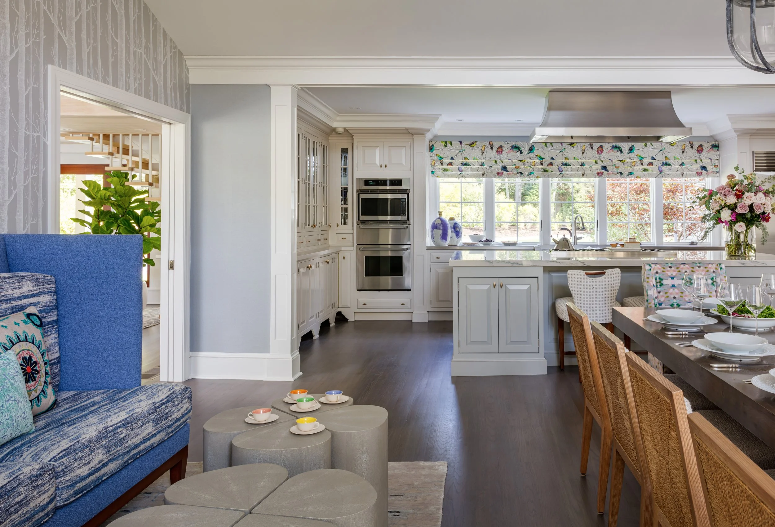 elegant open‑plan kitchen and dining space with white cabinets, colorful valances, blue accent seating, and wood table for modern home design inspiration