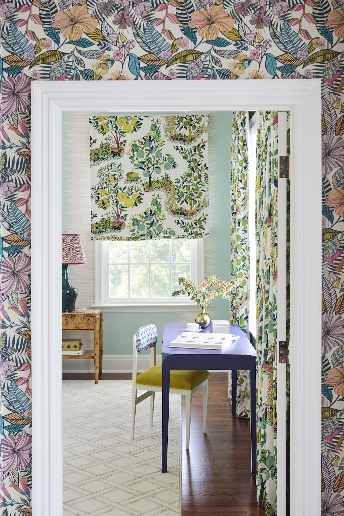 vibrant doorway view with tropical floral wallpaper outside citrus orchard roman shade and curtains purple lacquered desk by betsy wentz