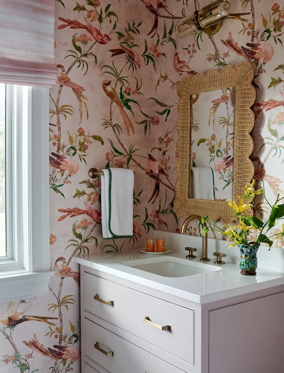 Blush bathroom bird wallpaper wicker scalloped mirror brass faucet ombre roman shade quartz countertop 