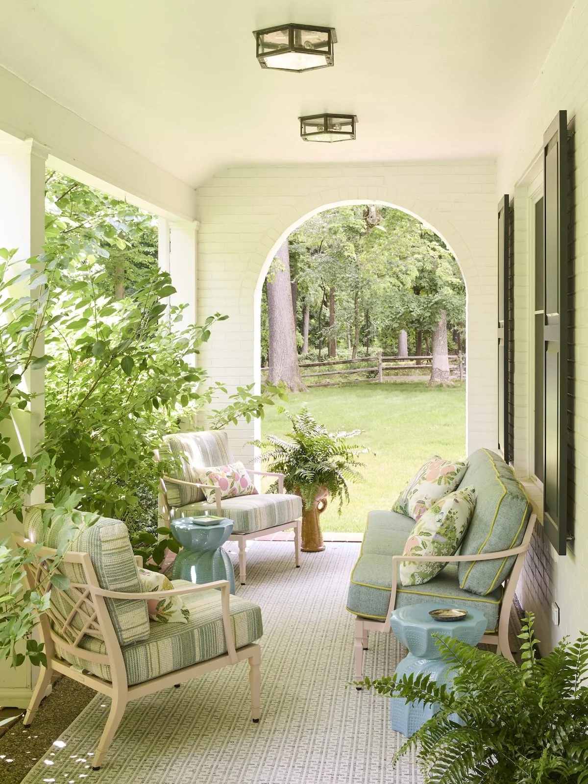 charming side porch seating with pastel striped armchairs aqua garden stools botanical pillows brick arch overlooking garden by betsy wentz