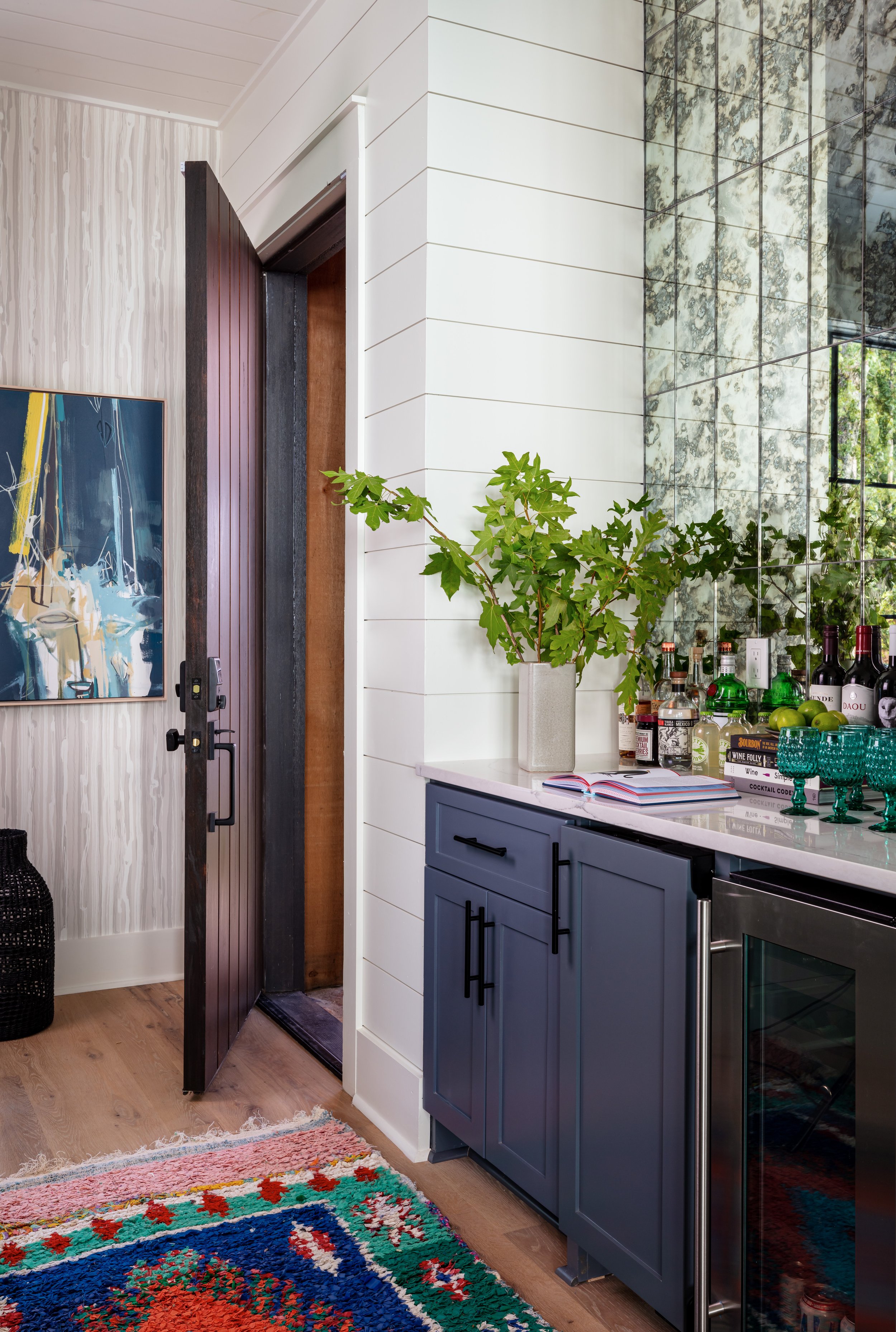 Stylish shiplap bar nook with dark blue cabinets, marble backsplash, colorful rug, and open door leading to modern interior design showcase