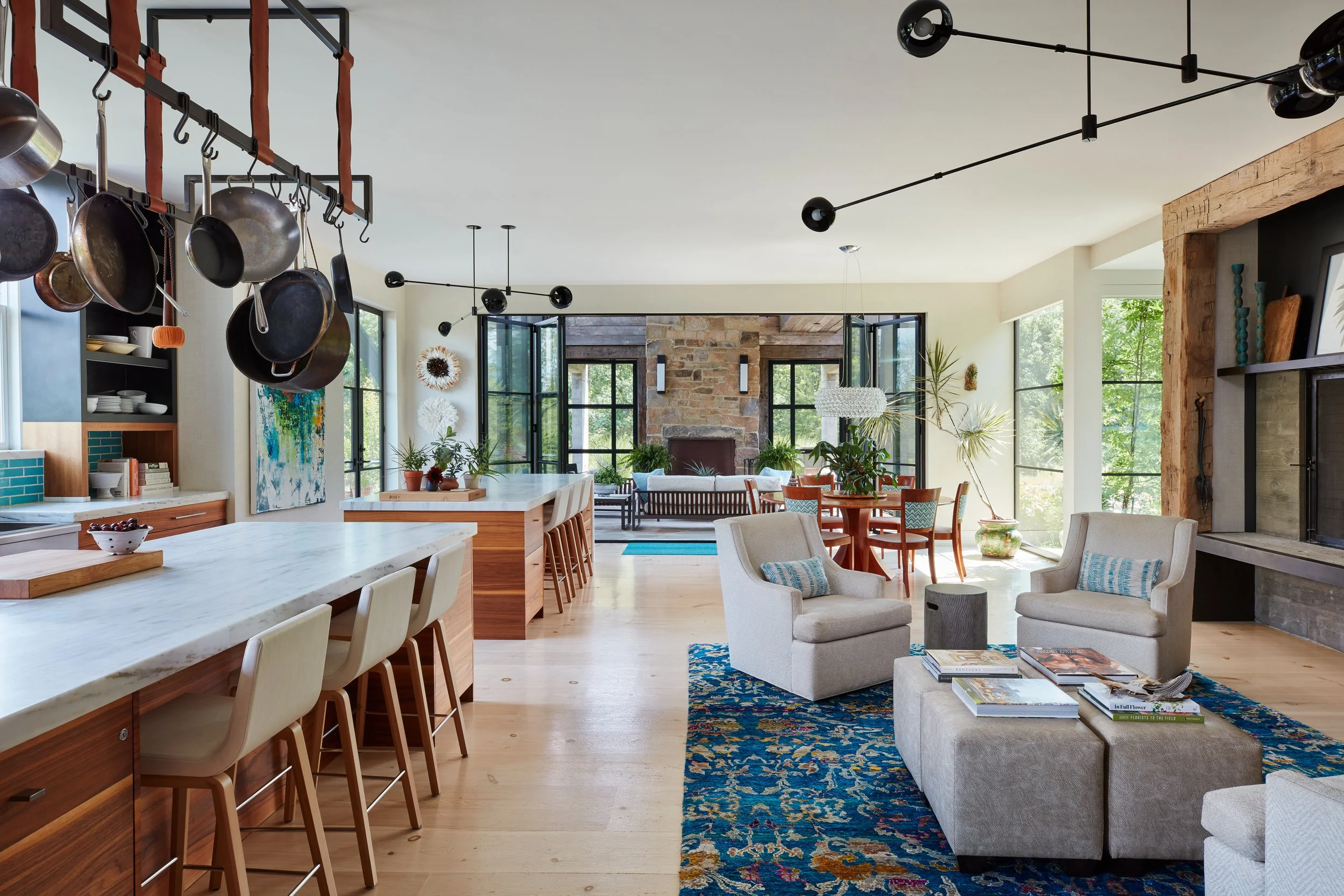 open-concept-kitchen-and-living-room-design-showcasing-rustic-modern-style-with-white-marble-island-wooden-stool-chairs-hanging-pots-pans-industrial-lighting-blue-patterned-rug-cozy-seating-area-large-windows-natural-light-exposed-brick-fireplace-interior.jpg