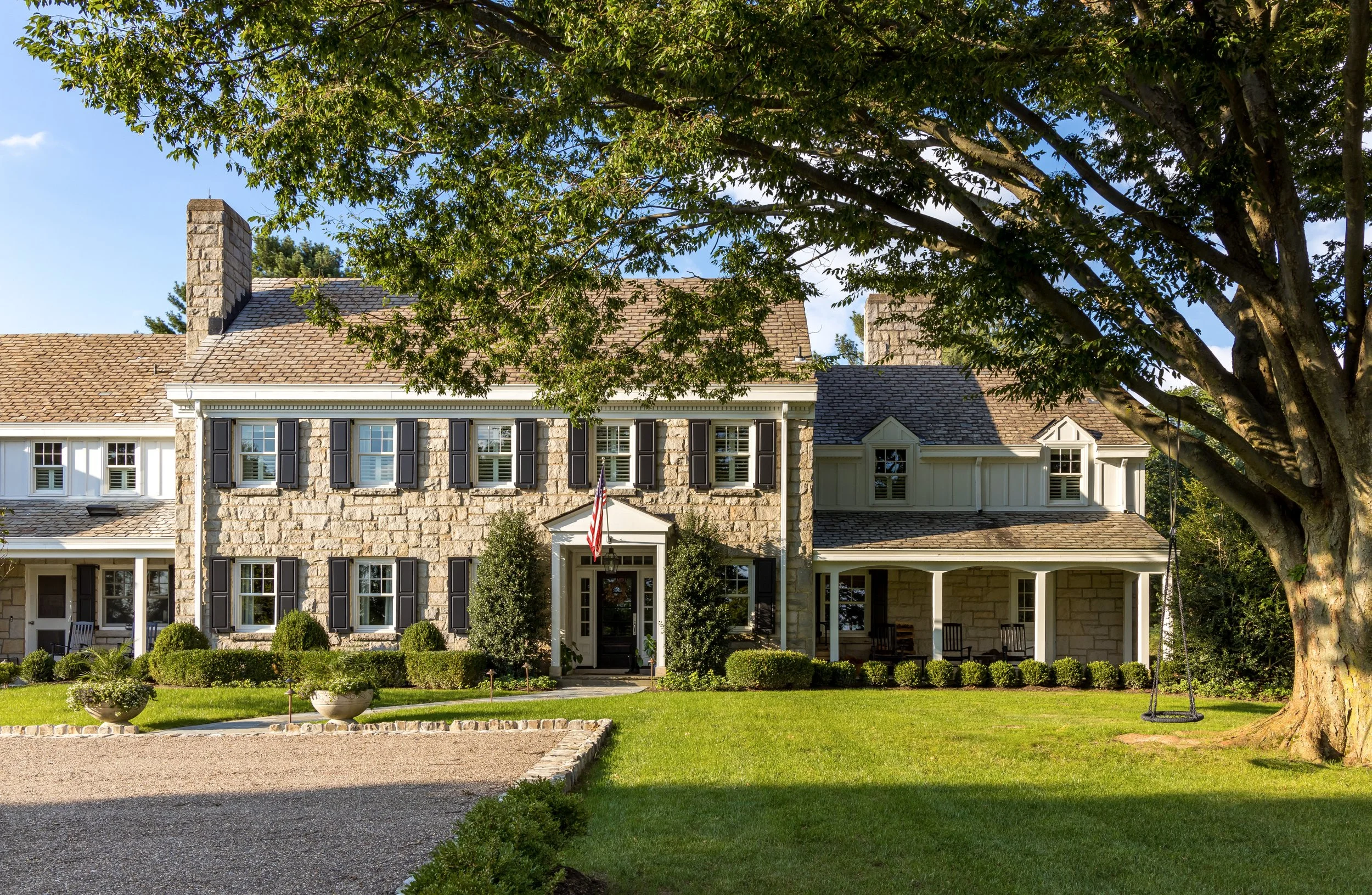 traditional stone home with black shutters in lush green setting with trees and. green grass