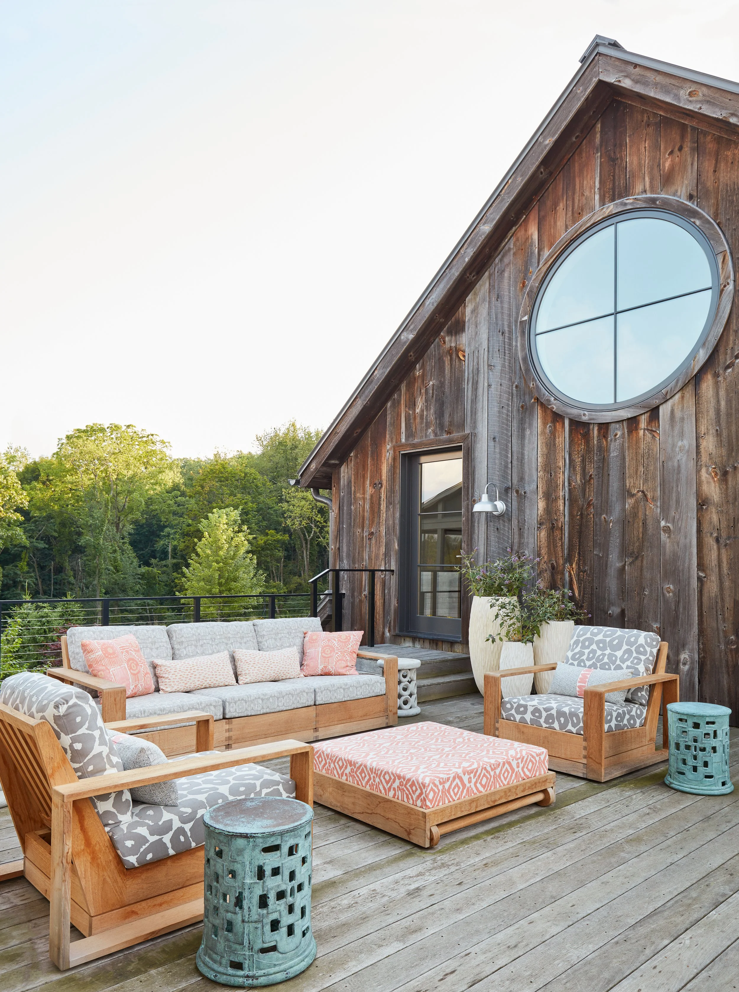 rustic-modern-patio-with-wood-barn-circular-window-light-wood-furniture-patterned-cushions-pink-accent-farmhouse-style-outdoor-design-inspiration.jpg