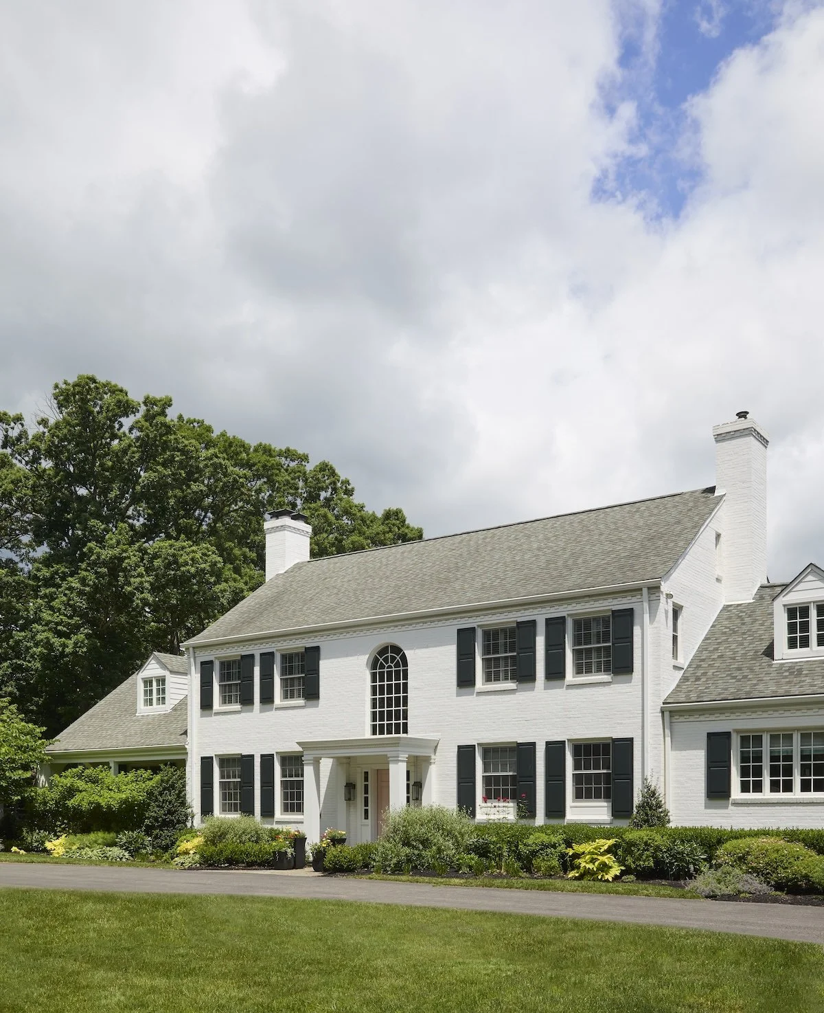 stately Pittsburgh white brick colonial with black shutters tall arched window blush front door lush landscaping