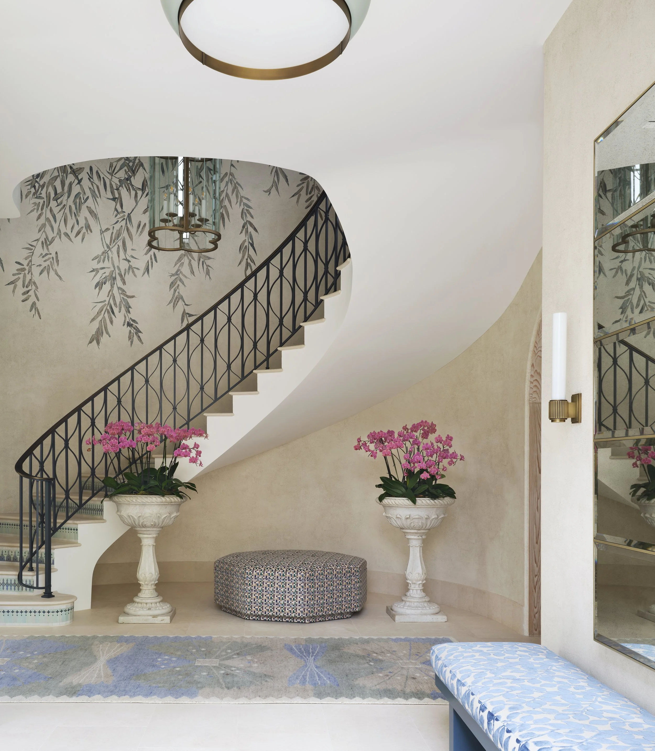 curved staircase design beige walls black metal railing pink orchids white urns patterned ottoman blue cushioned bench mirrored entryway