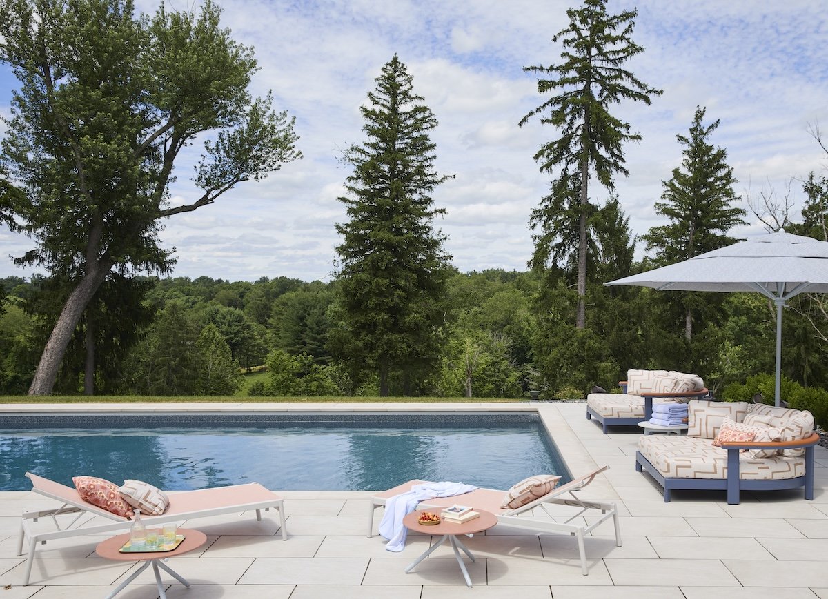 Serene poolside terrace with blush lounge chairs, patterned daybeds, stone pavers, lush tree overlook by Betsy Wentz design