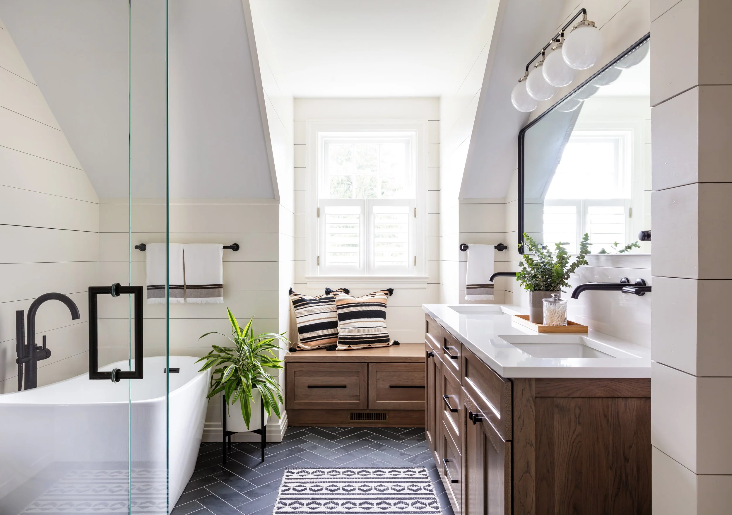 Modern farmhouse bathroom design featuring a sleek freestanding tub, double vanity with wood cabinets, black fixtures, and shiplap accents for stylish home renovation