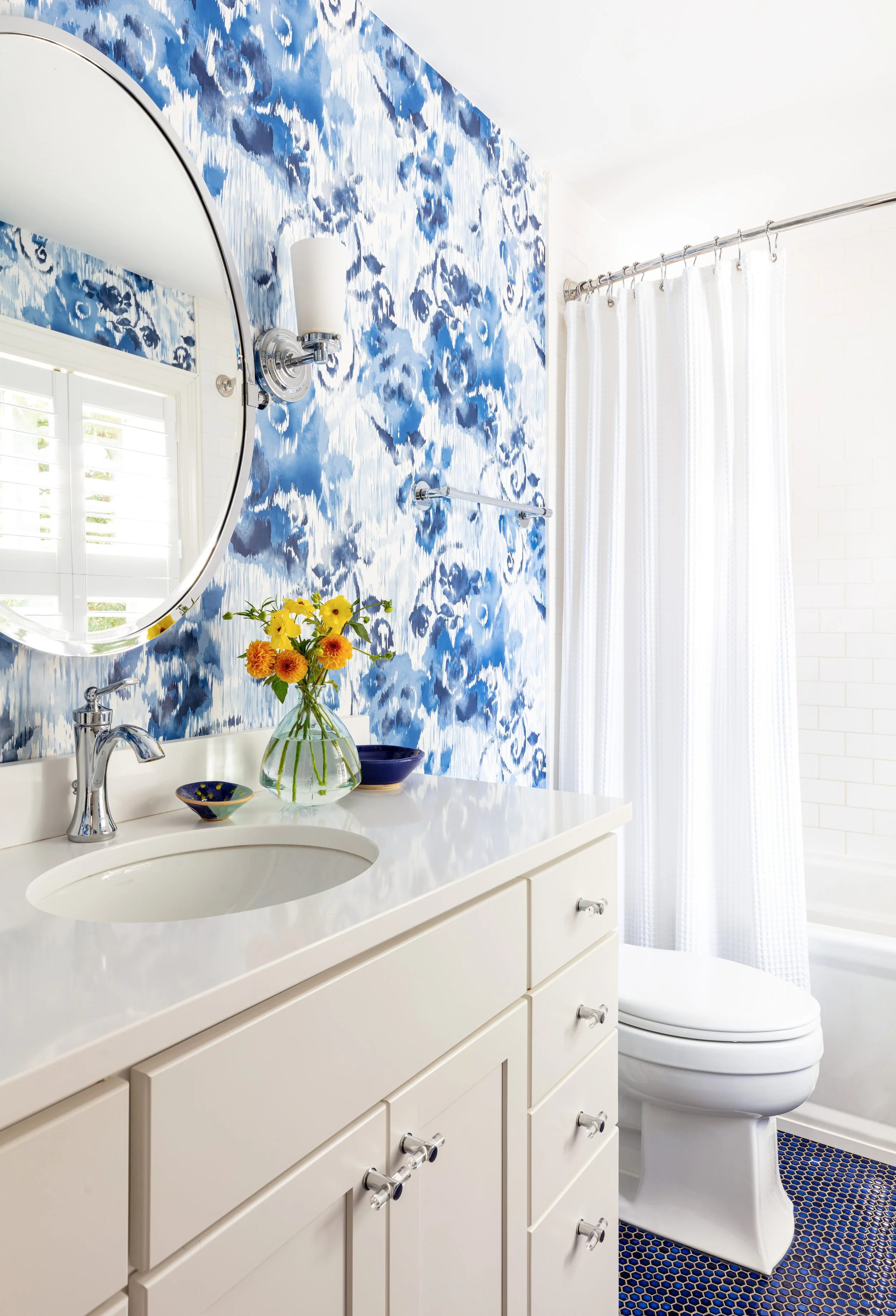 Blue floral wallpaper bathroom renovation with white vanity, round mirror, and chic accessories for stylish home design inspiration and modern interior updates
