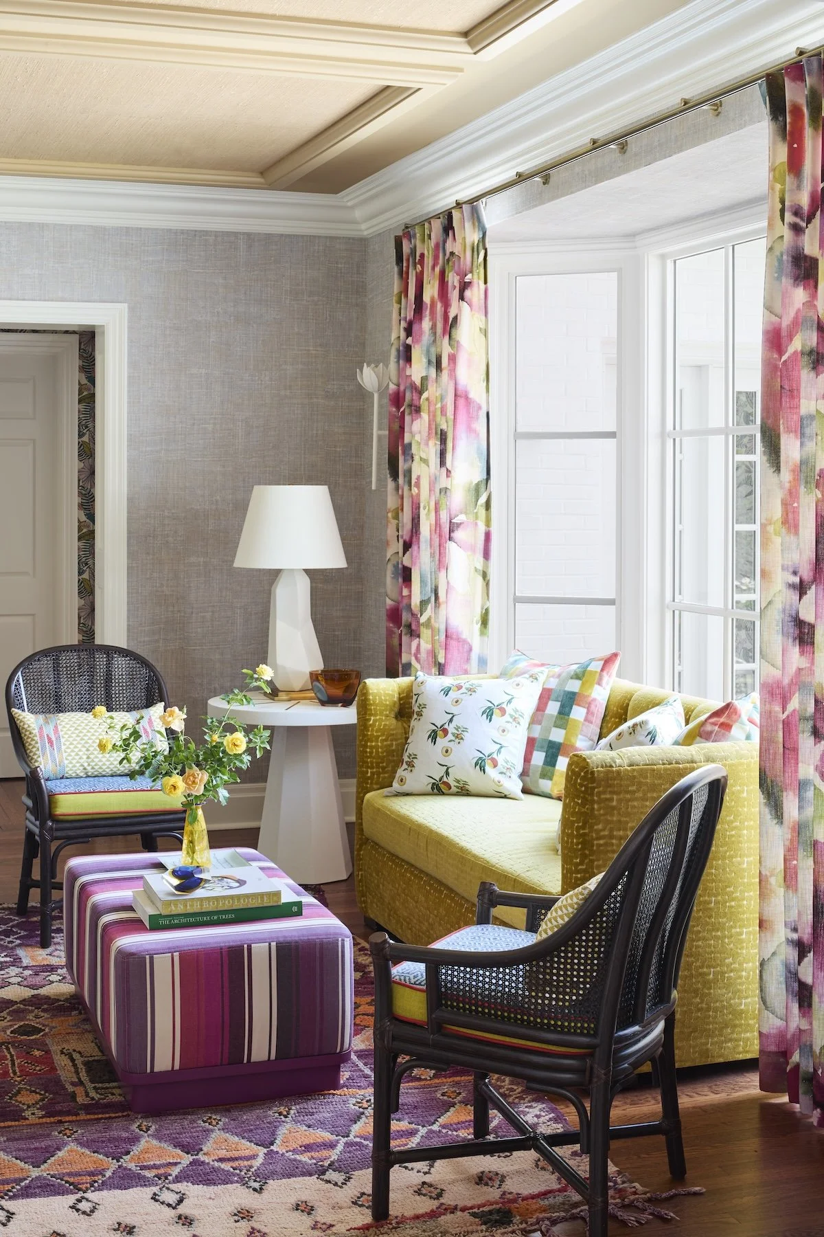 vibrant bay window sitting room with chartreuse tuxedo sofa, watercolor curtains, striped magenta ottoman, cane chairs and layered rugs by Betsy Wentz