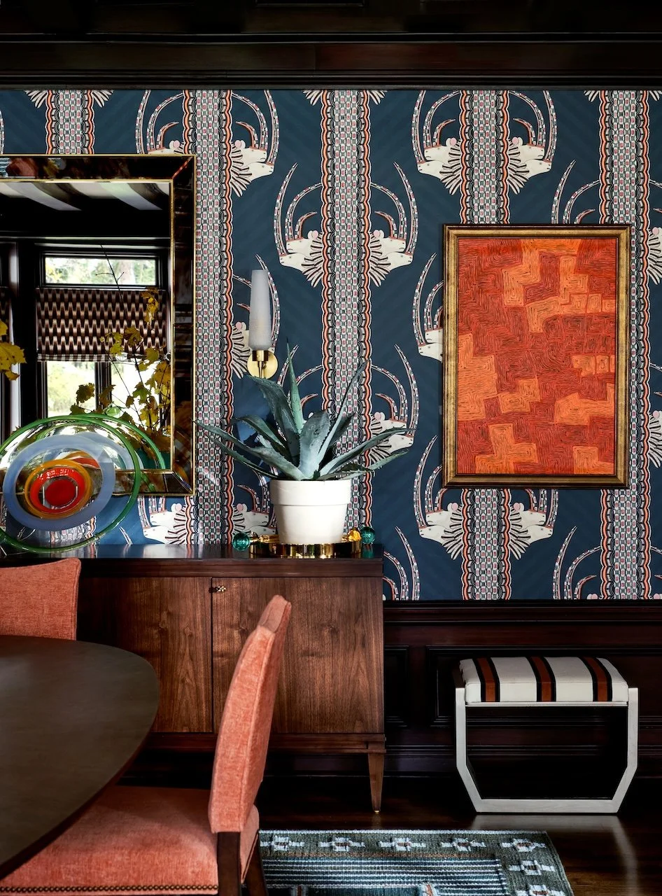 Eclectic dining room antelope wallpaper walnut sideboard coral chairs modern art striped bench brass accents