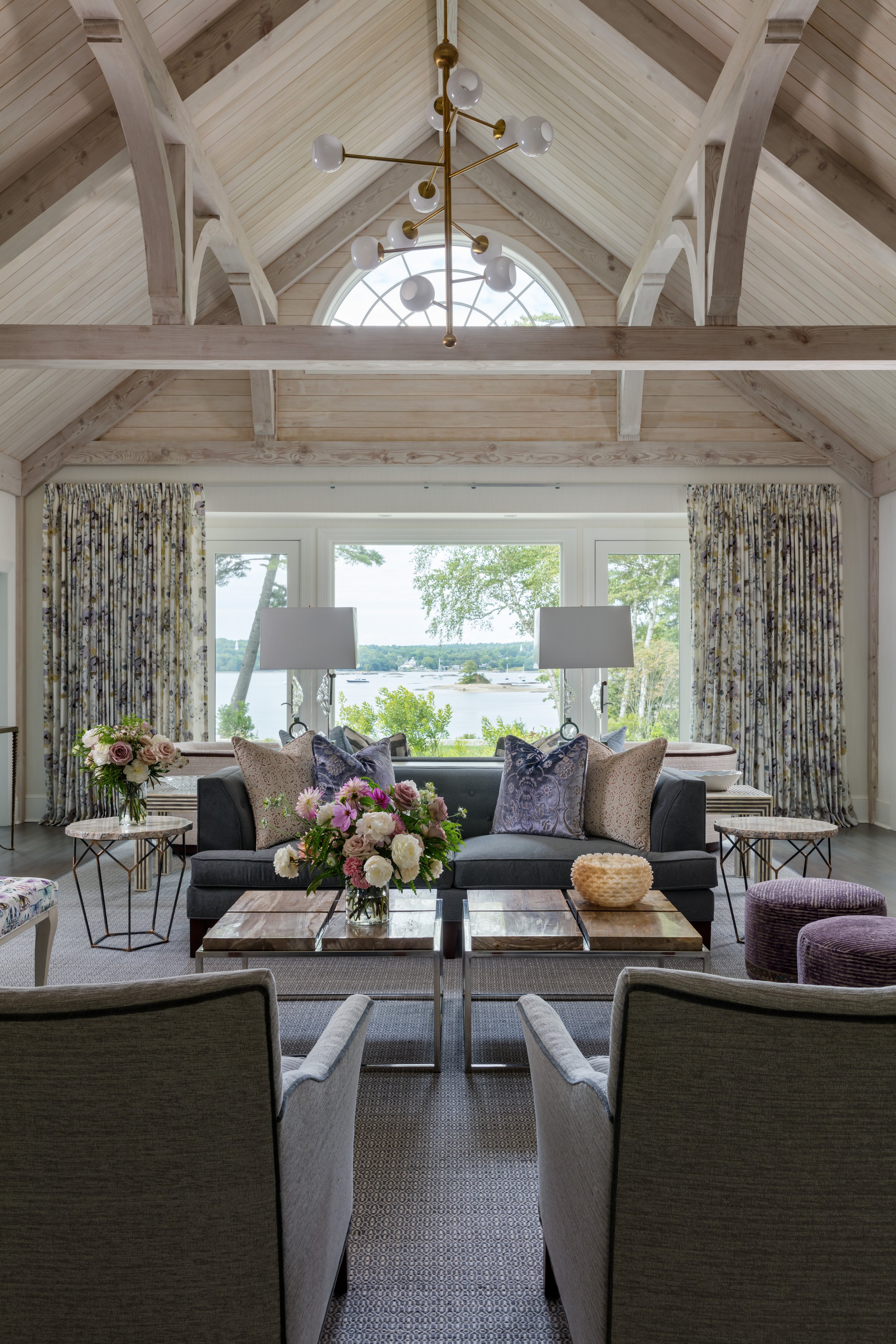 elegant waterside living room with vaulted wood ceiling, modern chandelier, gray sofa, floral accents stylish furnishings for cozy retreat