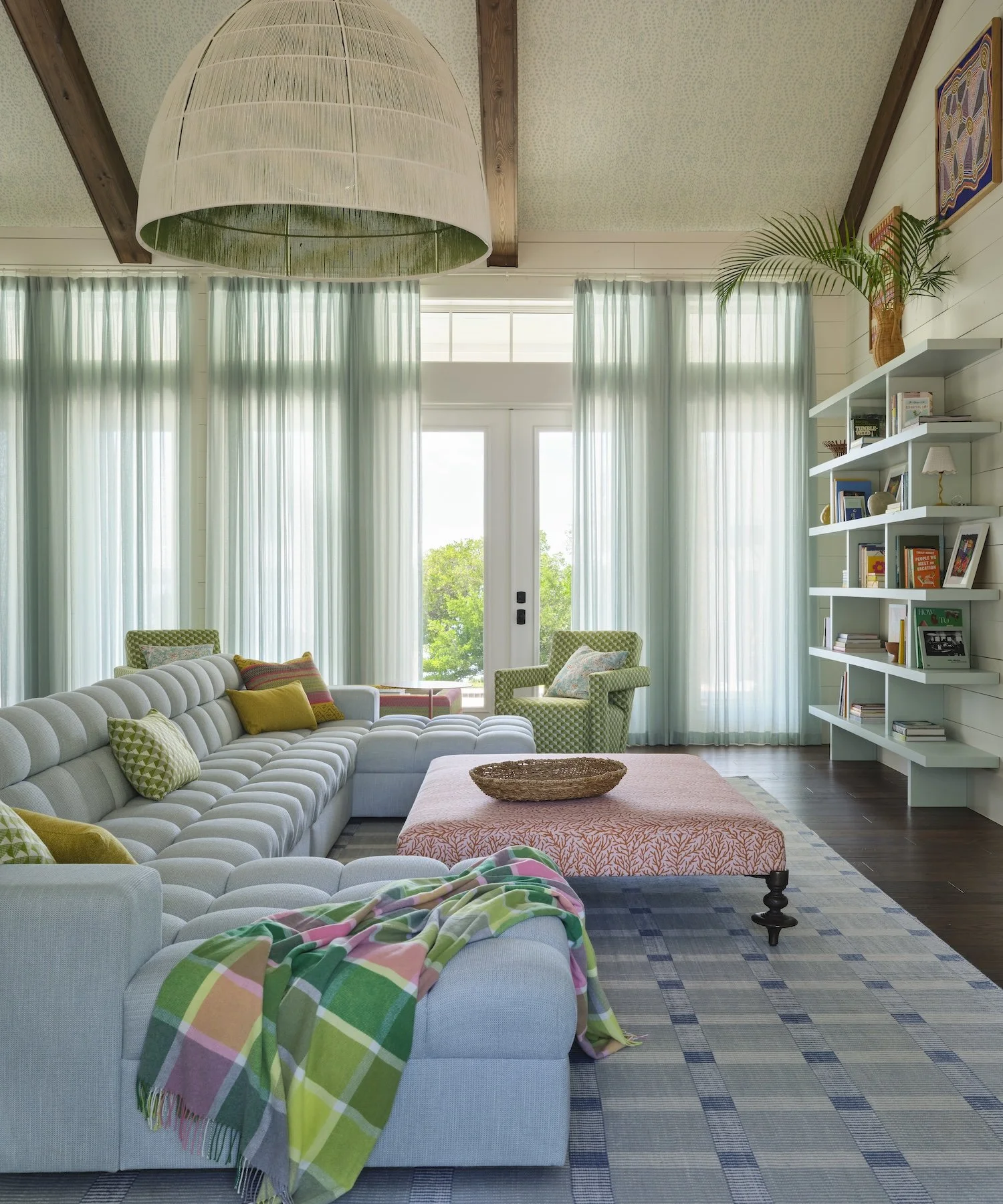 12-lorida-living-room-sectional-sofa-patterned-ottoman-blue-shelves-sheer-curtains-vibrant-coastal-design.jpg