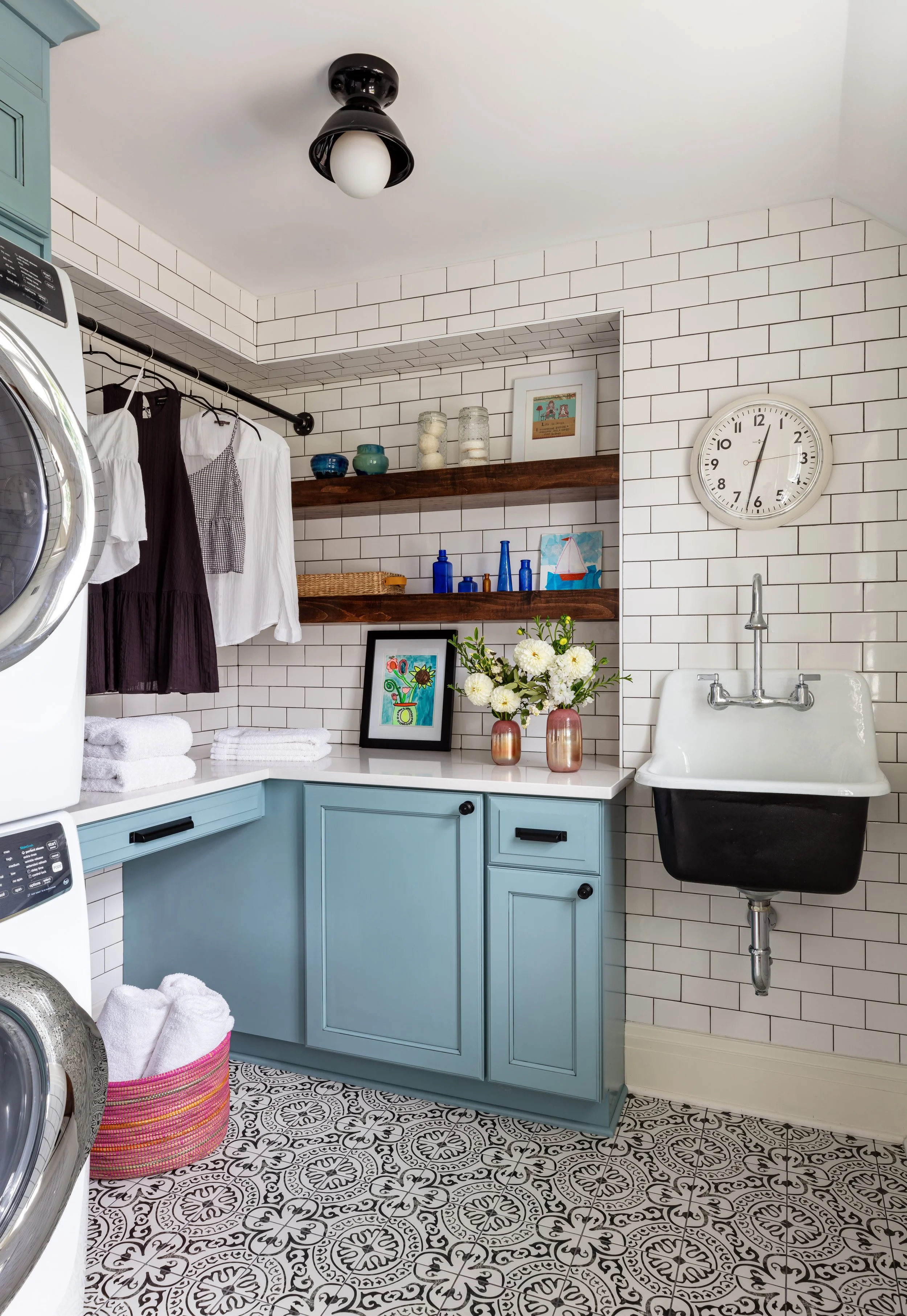 functional laundry room with blue painted cabinets stacked washer and dryer and farmhouse sink