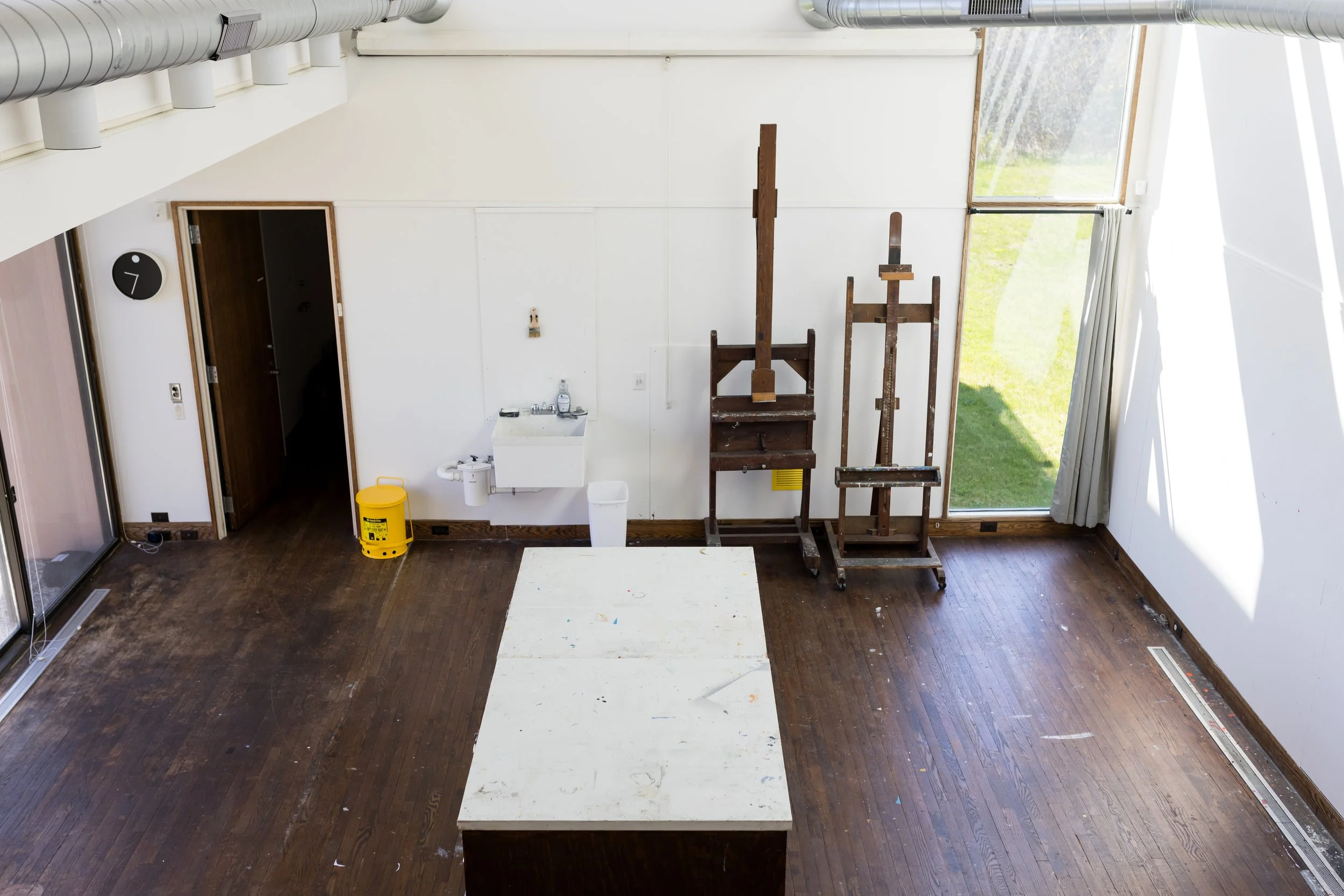 Art studio interior with easels, a work table, and a sink against a white wall.