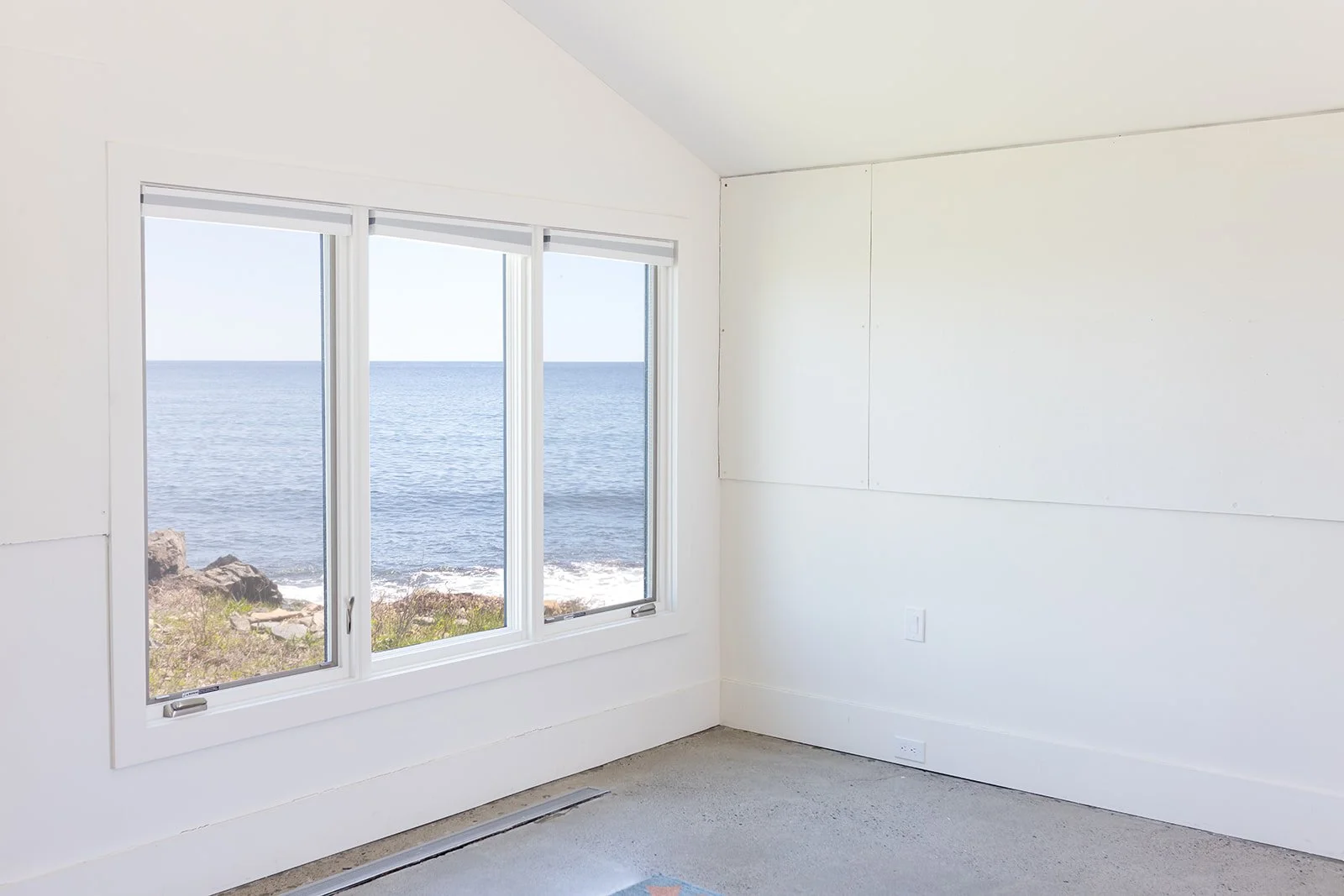 View of minimalist room with blank walls and terrazzo floors, facing large windows that look to the ocean.