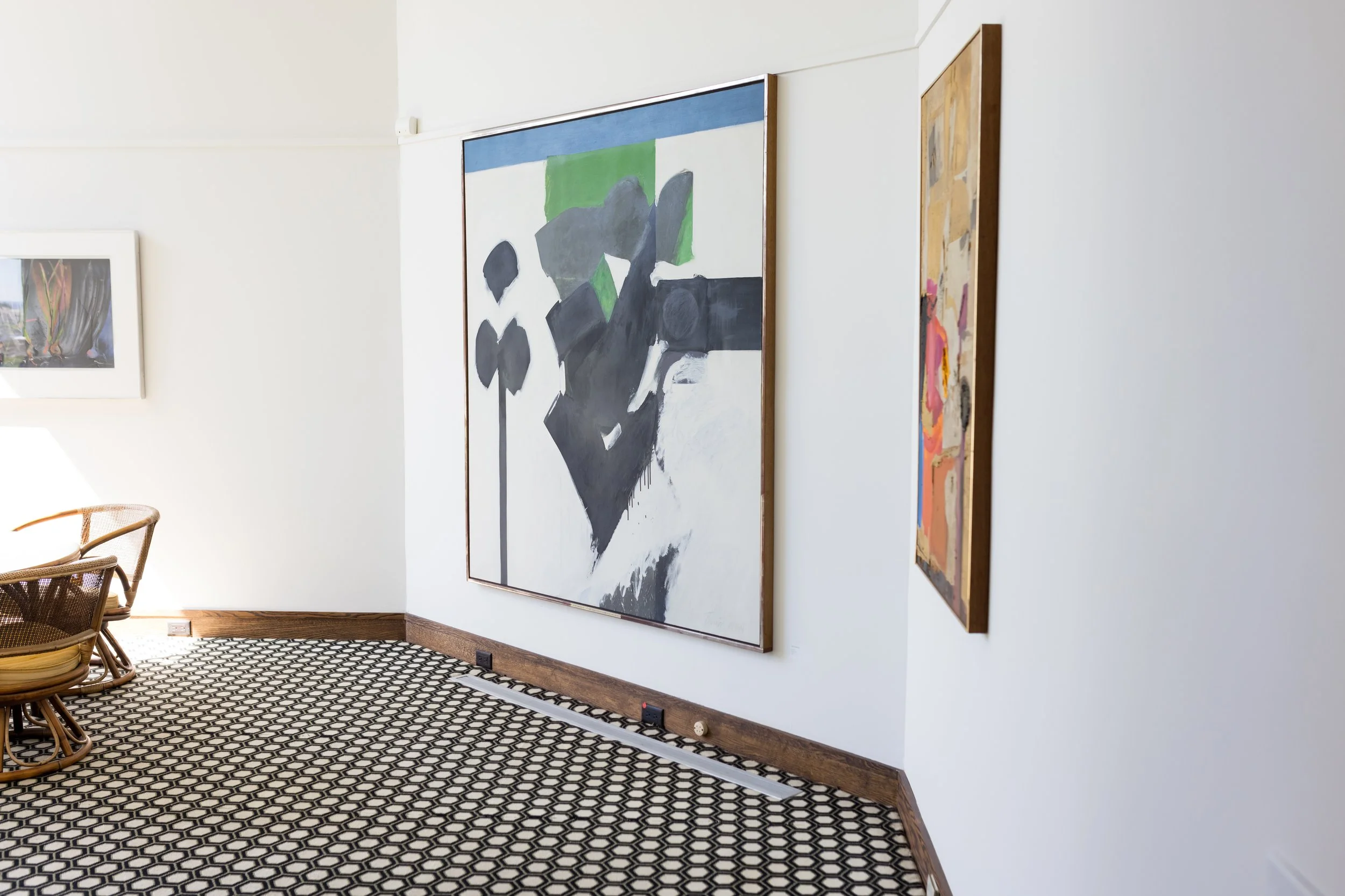 Room with abstract paintings on white walls, wicker chairs, and hexagonal patterned flooring.