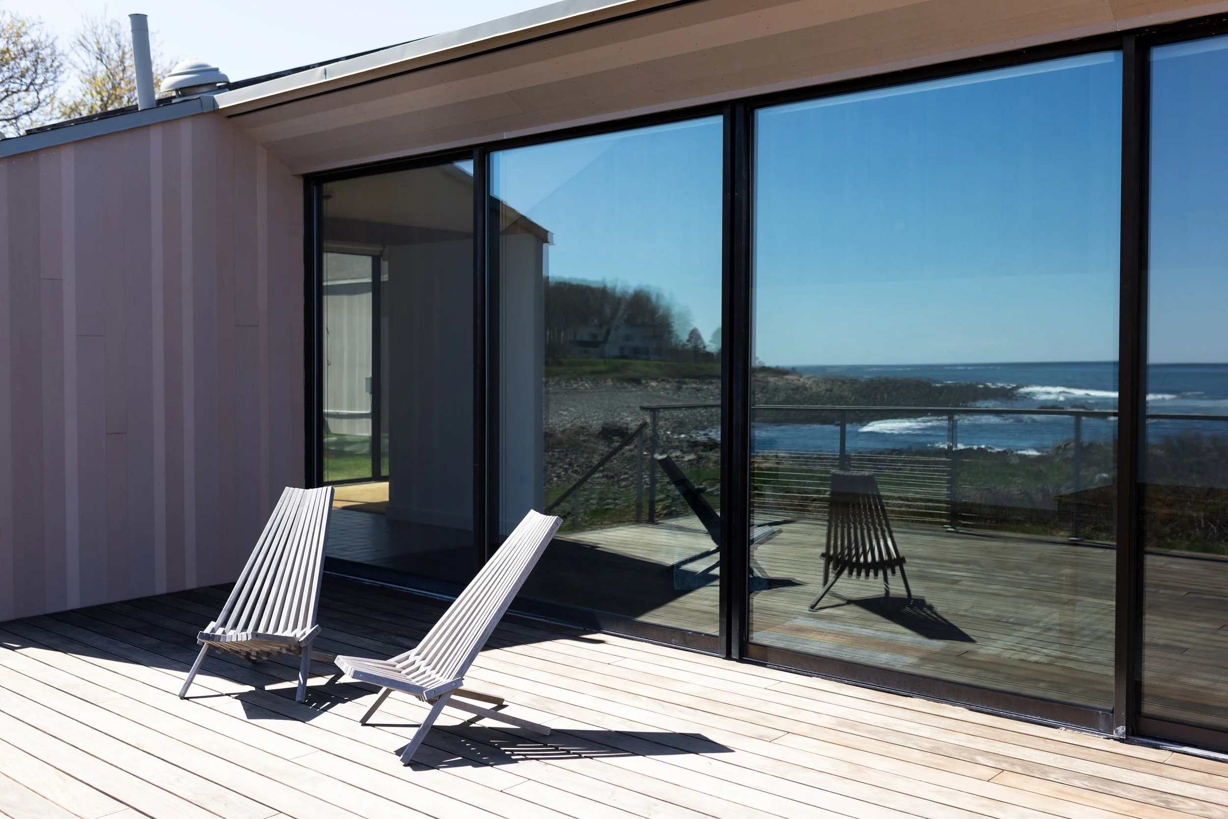 Modern patio with two chairs and ocean view, reflected in glass doors.