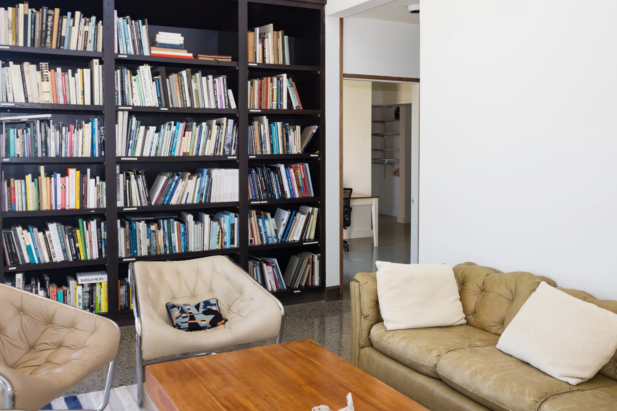 Living room with bookshelves, brown leather couch, chairs, and wooden coffee table.