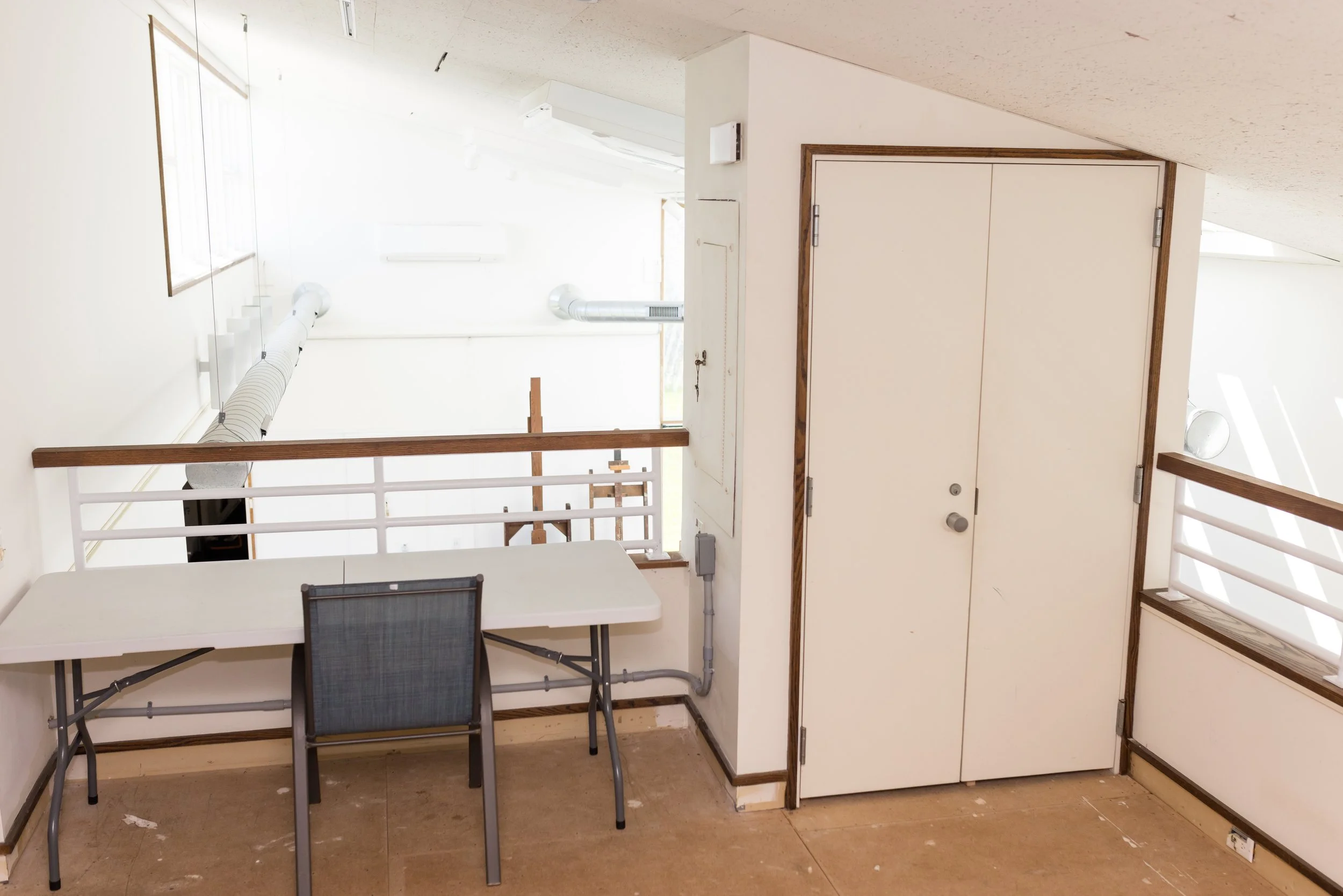 Interior loft space with a folding table, chair, and railing. Ducts are visible on the ceiling.
