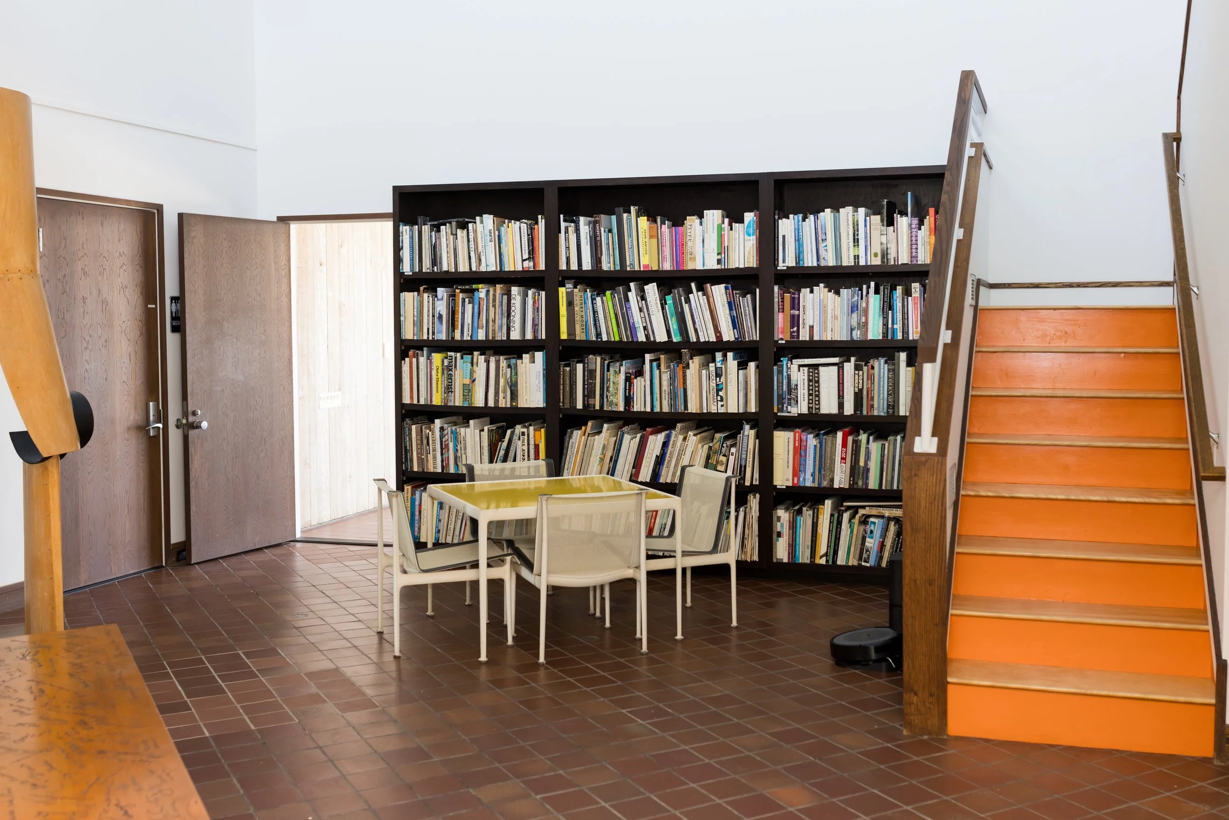 Room with bookshelves, orange stairs, table, and chairs.