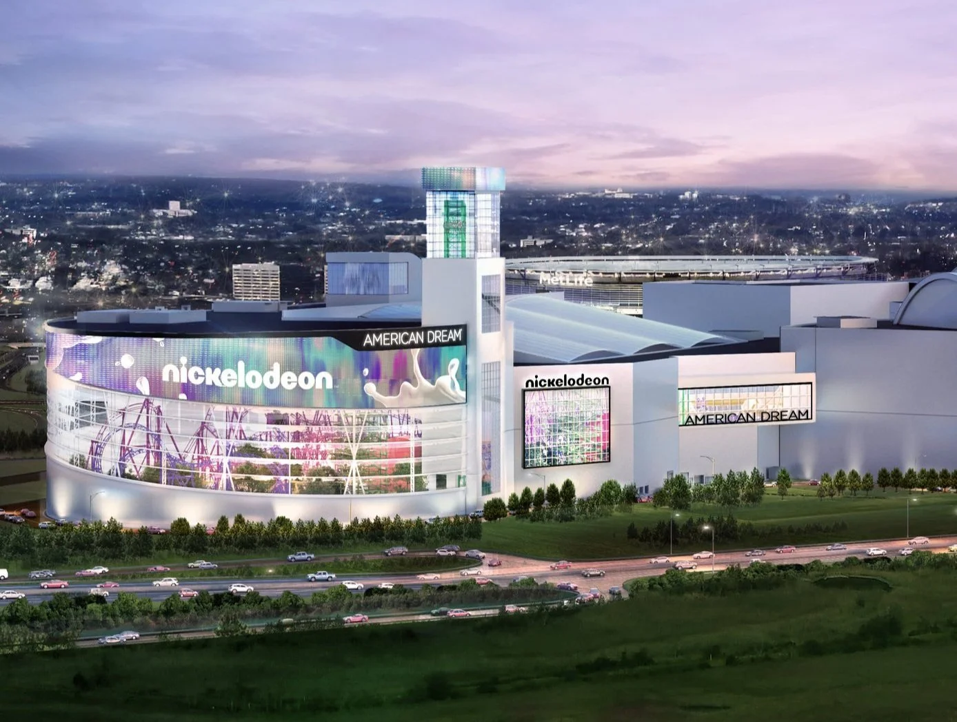 Colorful modern building with large digital billboards displaying Nickelodeon and American Dream logos, situated along a highway with cars, surrounded by greenery and with a cityscape background at dusk.