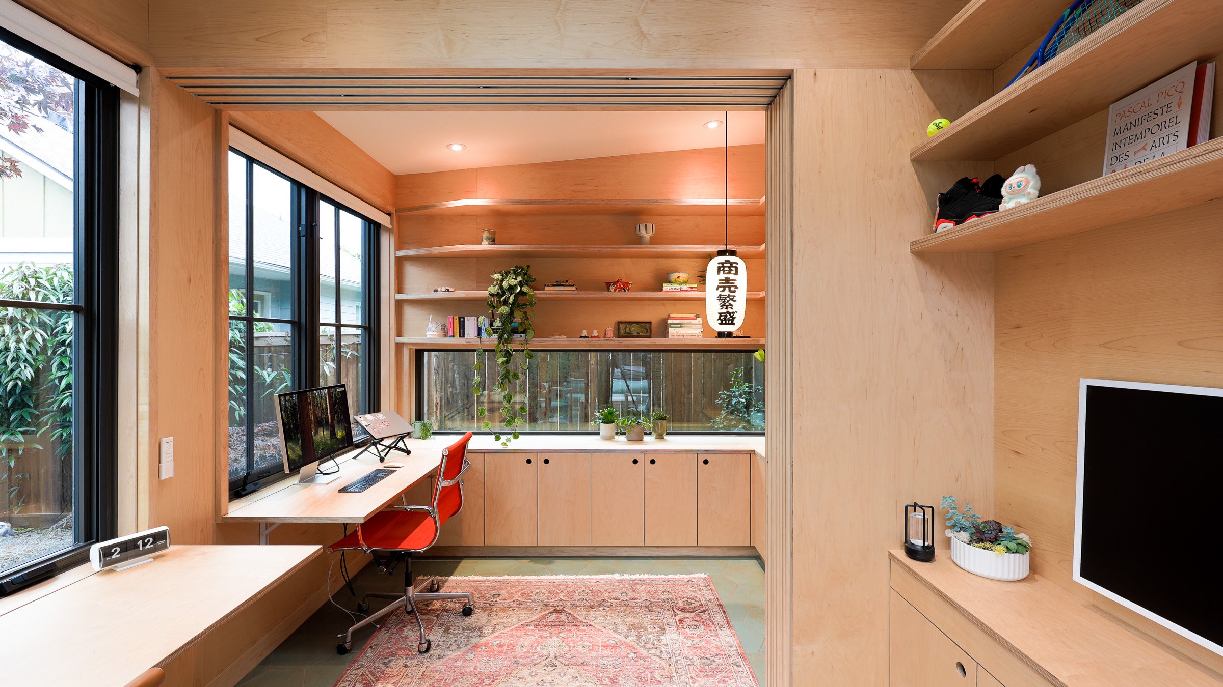 Interior view of a custom backyard office by Seahaus Architecture, showing built-in desks, Europly cabinetry, open shelving, and a sliding partition.