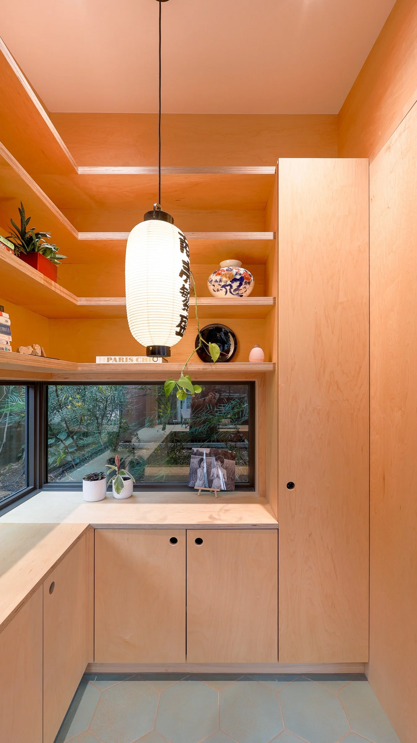 Interior detail of a backyard office by Seahaus Architecture, featuring wood shelving, pendant lantern, and garden-facing window.